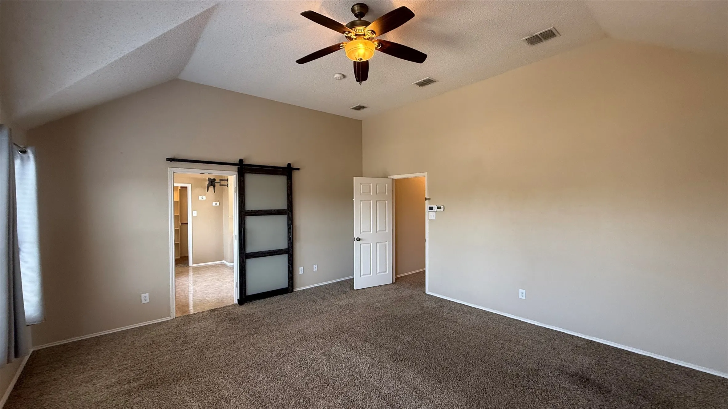 Vaulted ceiling with a ceiling fan, carpeted flooring, and a sliding barn door with frosted glass panels