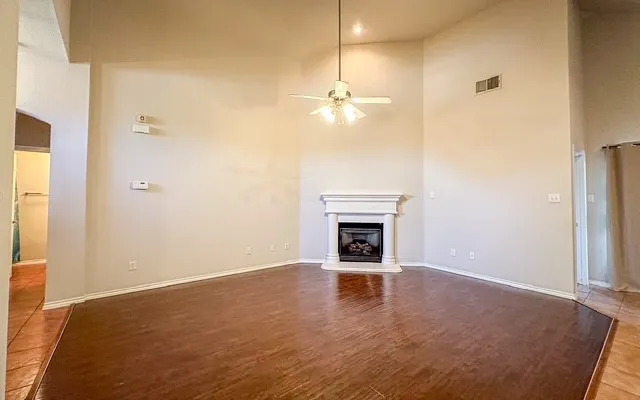 Wood-finish flooring, vaulted ceiling, traditional fireplace with mantel, ceiling fan with integrated lighting, and neutral wall tones