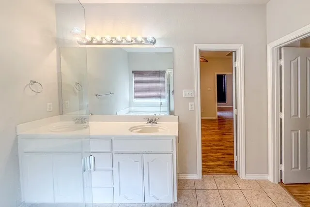 Double vanity with integrated sinks, white cabinetry, and a large mirror