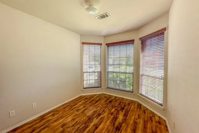 Bay window with three individual windows, wood-finish blinds, wood-finish flooring, and a flush mount light fixture