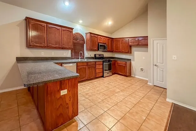 Kitchen featuring wood cabinetry, granite-finish countertops, stainless steel appliances, and tiled flooring