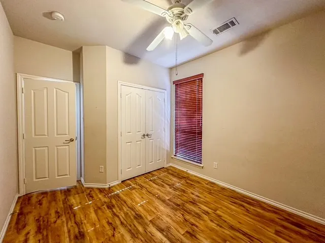 Wood-finish flooring with a ceiling fan, window with blinds, and white paneled doors