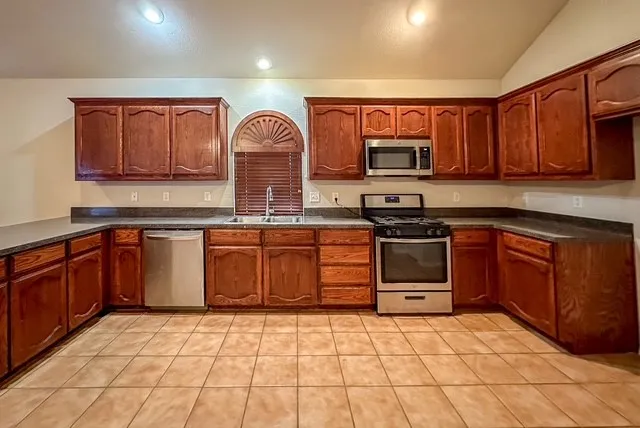 Kitchen featuring warm wood cabinetry, stainless steel appliances, dark countertops, and tile flooring
