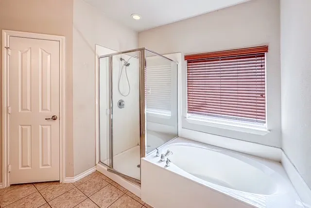 Recessed lighting, enclosed glass shower, built-in soaking tub, and tile flooring
