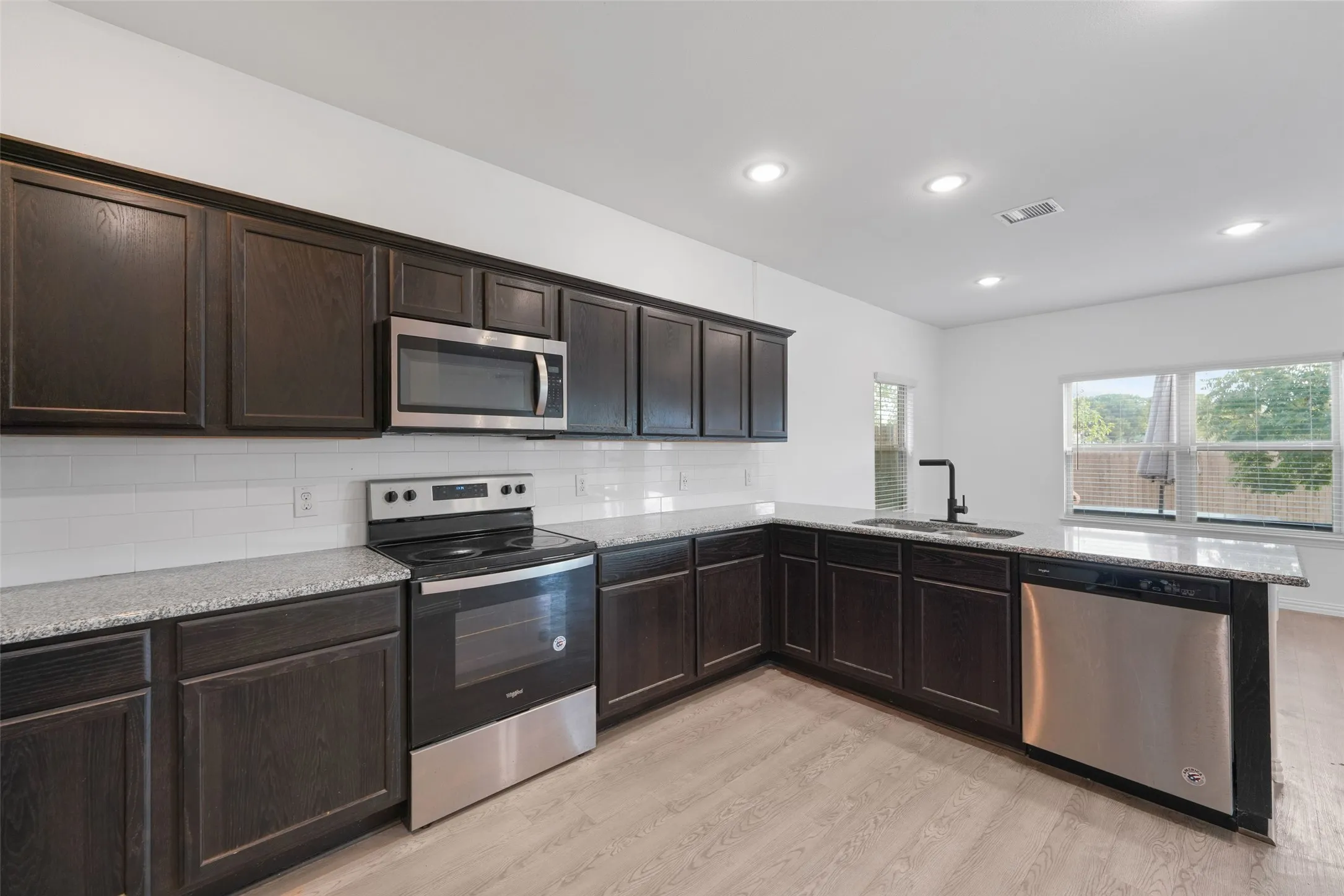 Modern kitchen featuring dark cabinetry with raised-panel doors, stainless steel appliances including a slide-in range and over-the-range microwave, quartz countertops, subway tile backsplash, and light wood-finish flooring