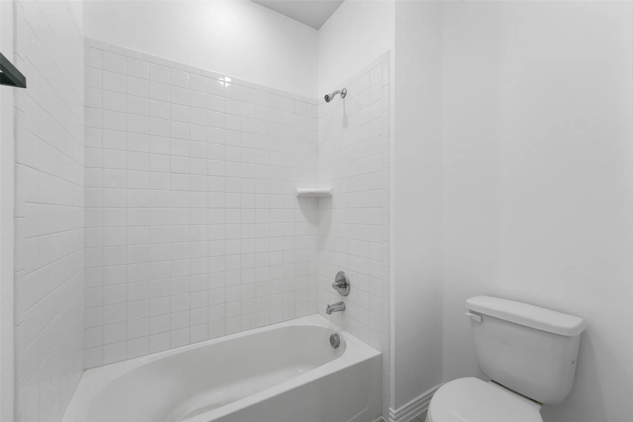 White tiled shower with built-in soap dish, chrome fixtures, and a white porcelain bathtub