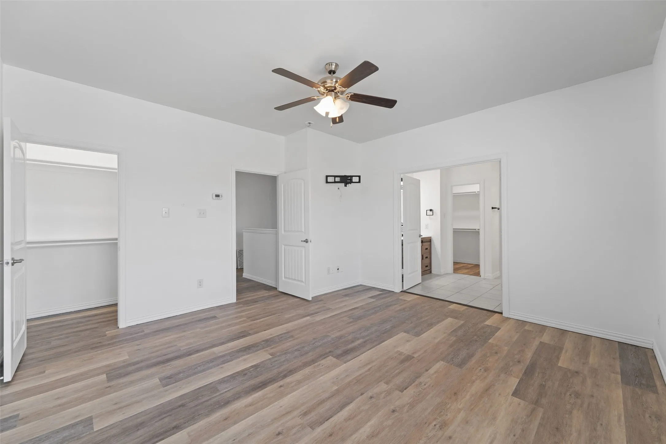 Wood-finish flooring, ceiling fan, white walls, and built-in closet shelving
