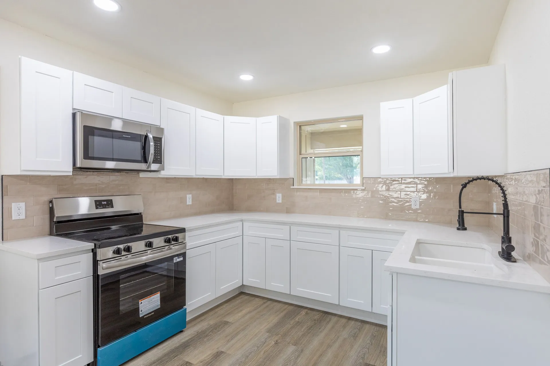 Kitchen featuring wood-finish flooring, white cabinetry, a stainless steel microwave and range, and light-toned backsplash tiling