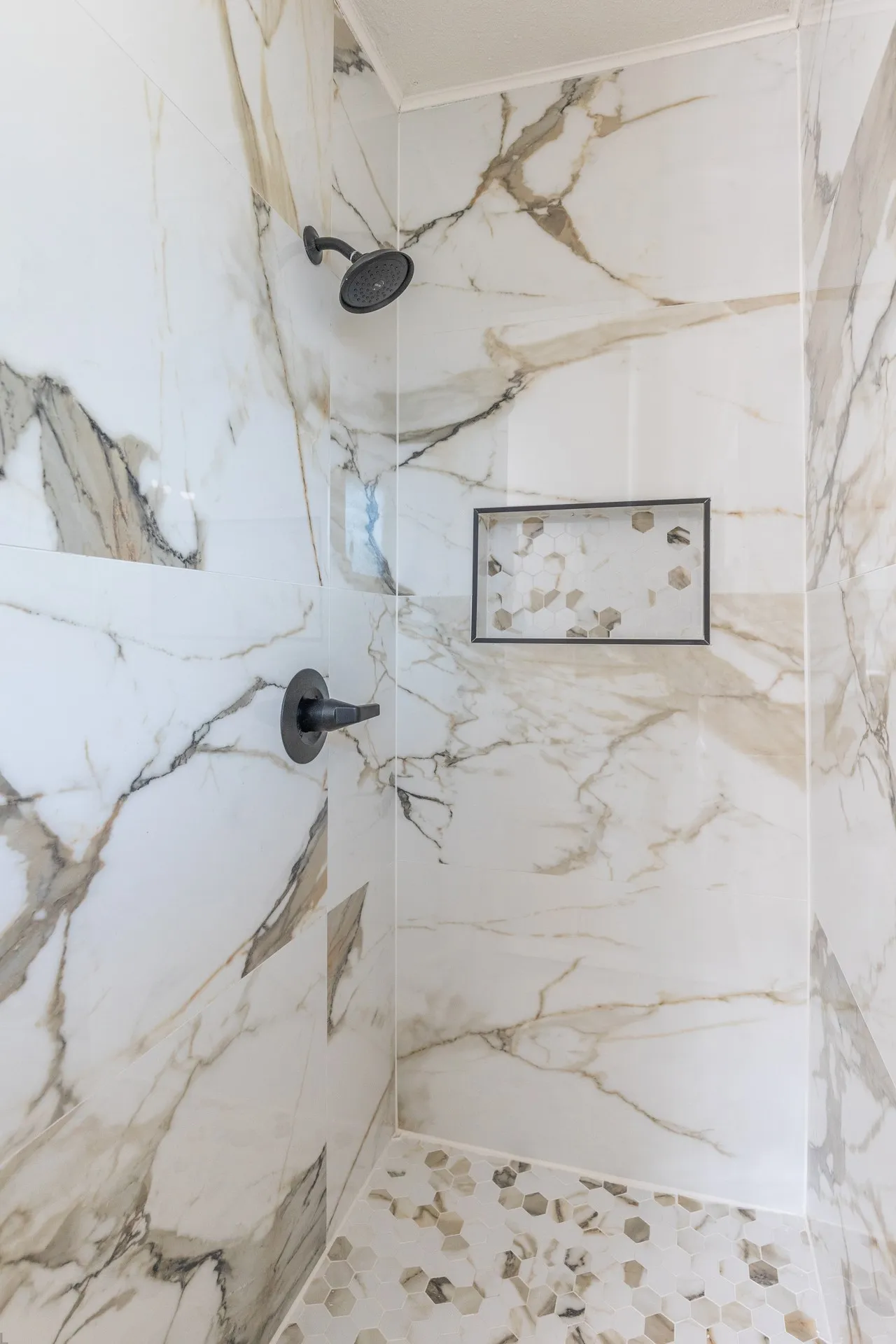 Shower with large format porcelain tile walls, matte black fixtures, an integrated shower niche, and a mosaic tile floor