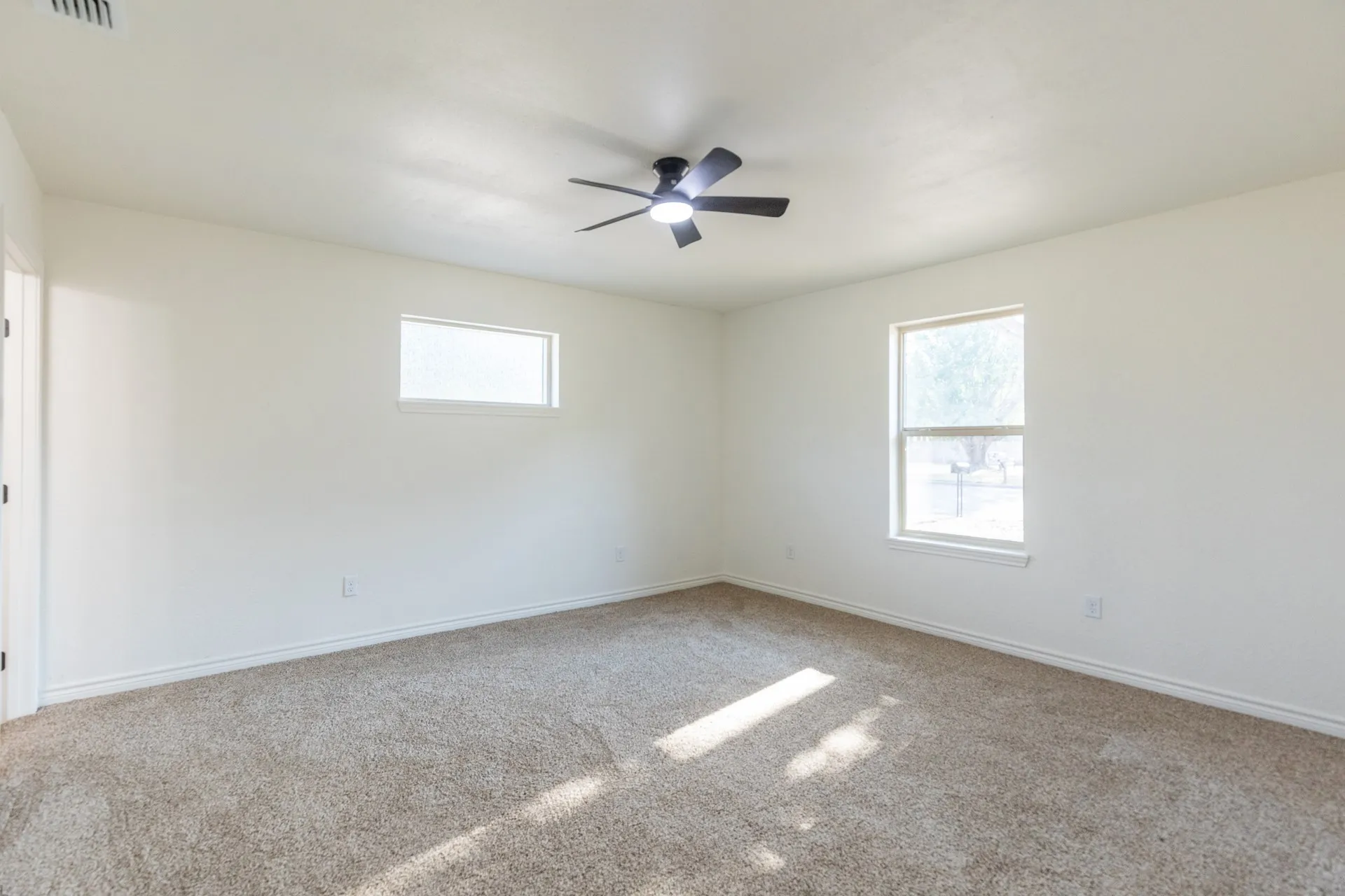 Neutral tone wall paint, carpet flooring, a ceiling fan with integrated lighting, and multiple windows