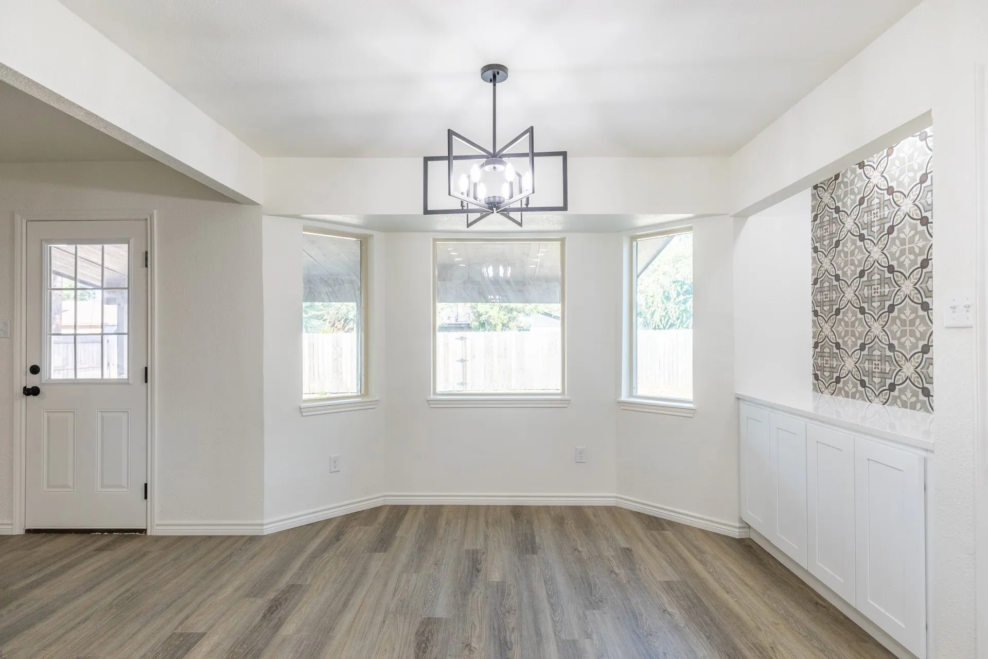 Room featuring wood-finish flooring, a modern geometric chandelier, a built-in cabinet with a countertop, and an accent wall with patterned tile