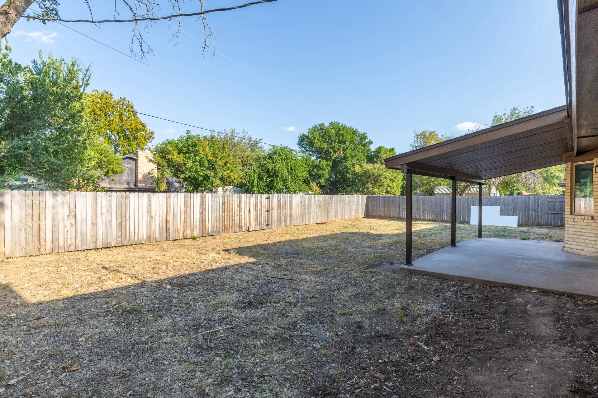 Expansive backyard featuring a wood fence, covered patio, concrete slab, and brick exterior