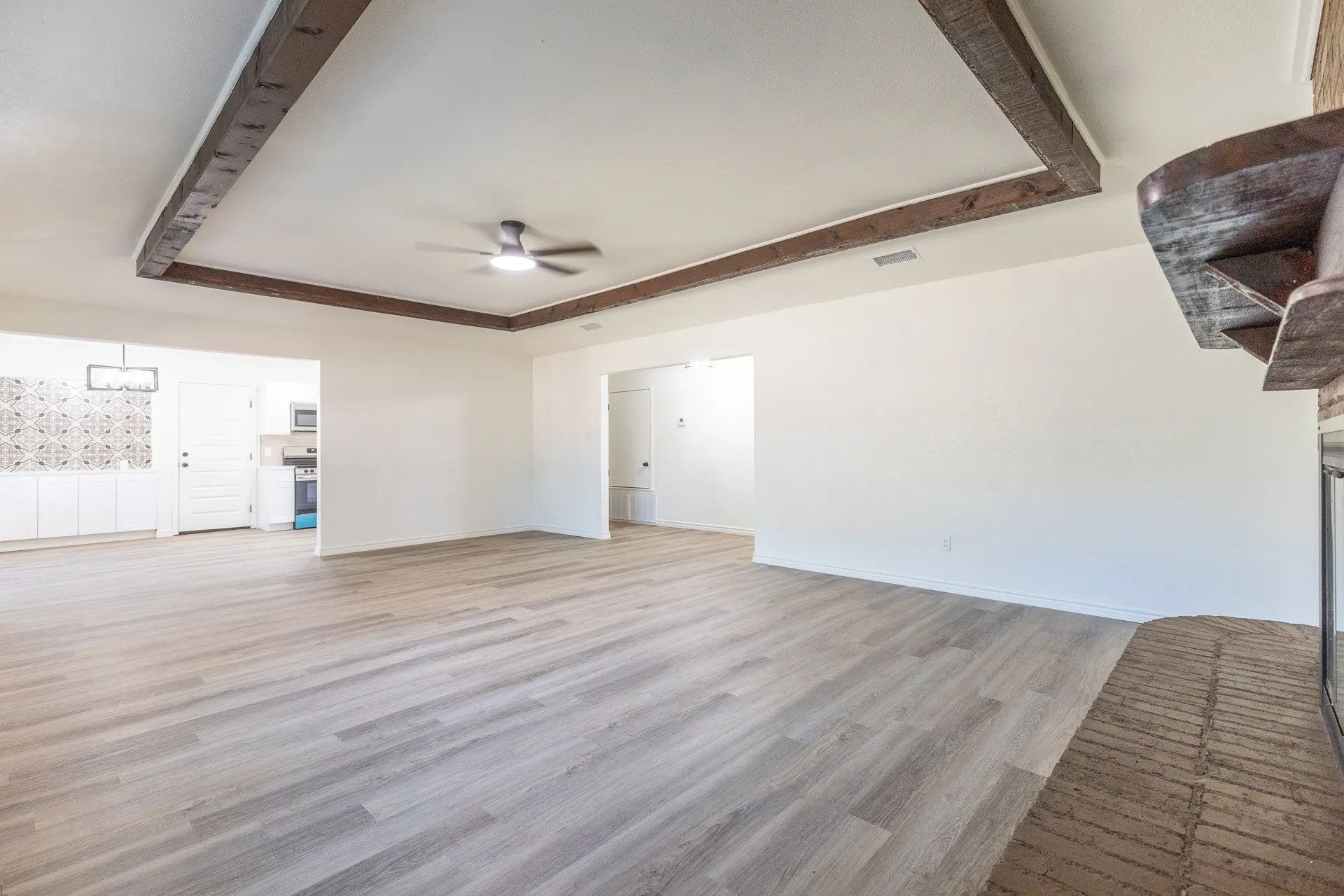 Wood-finish flooring, exposed wood ceiling beams, modern ceiling fan, white cabinetry, and decorative tile backsplash