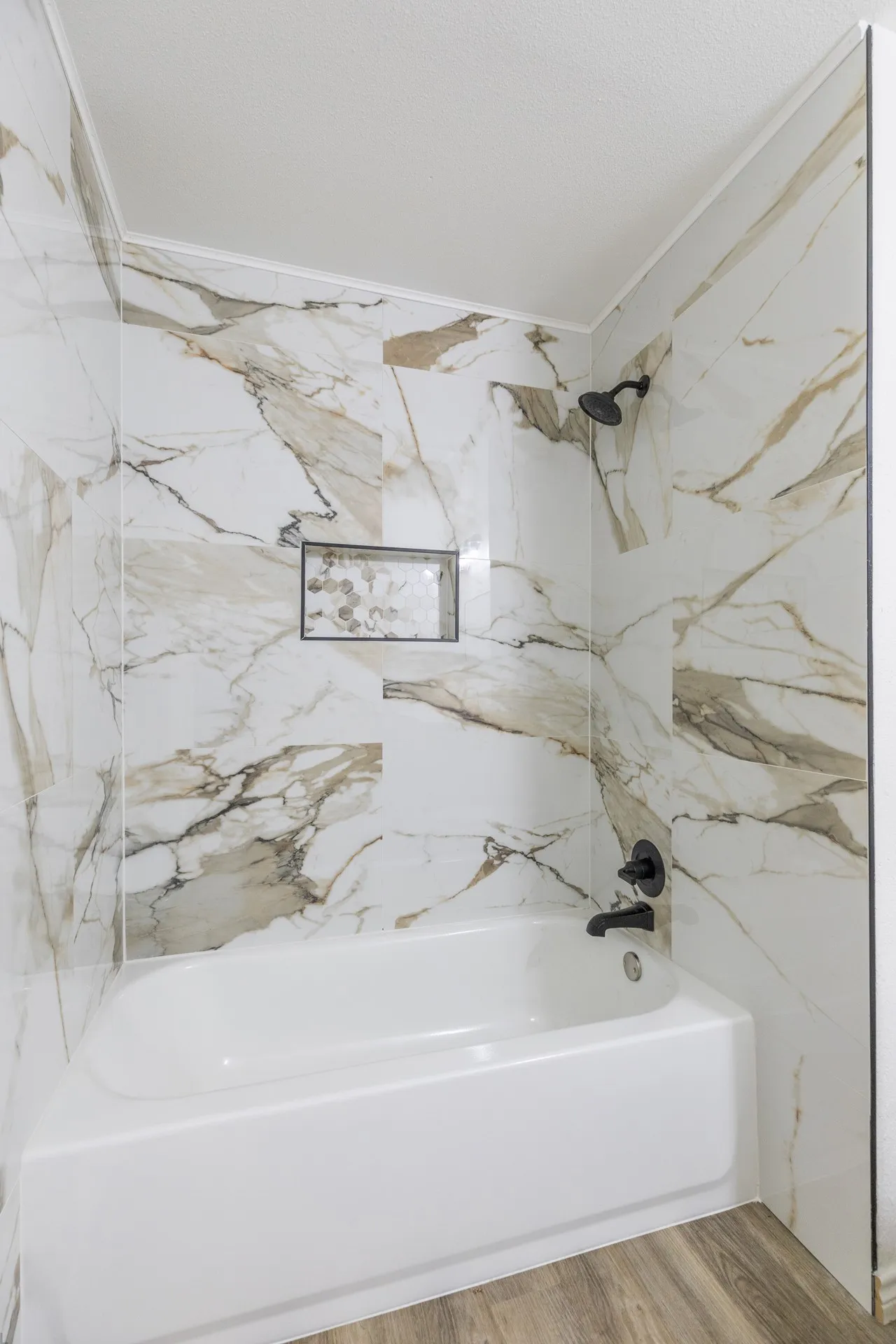 Bathtub with matte black fixtures, marble-look tile surround, and a recessed shower niche with mosaic tile accent