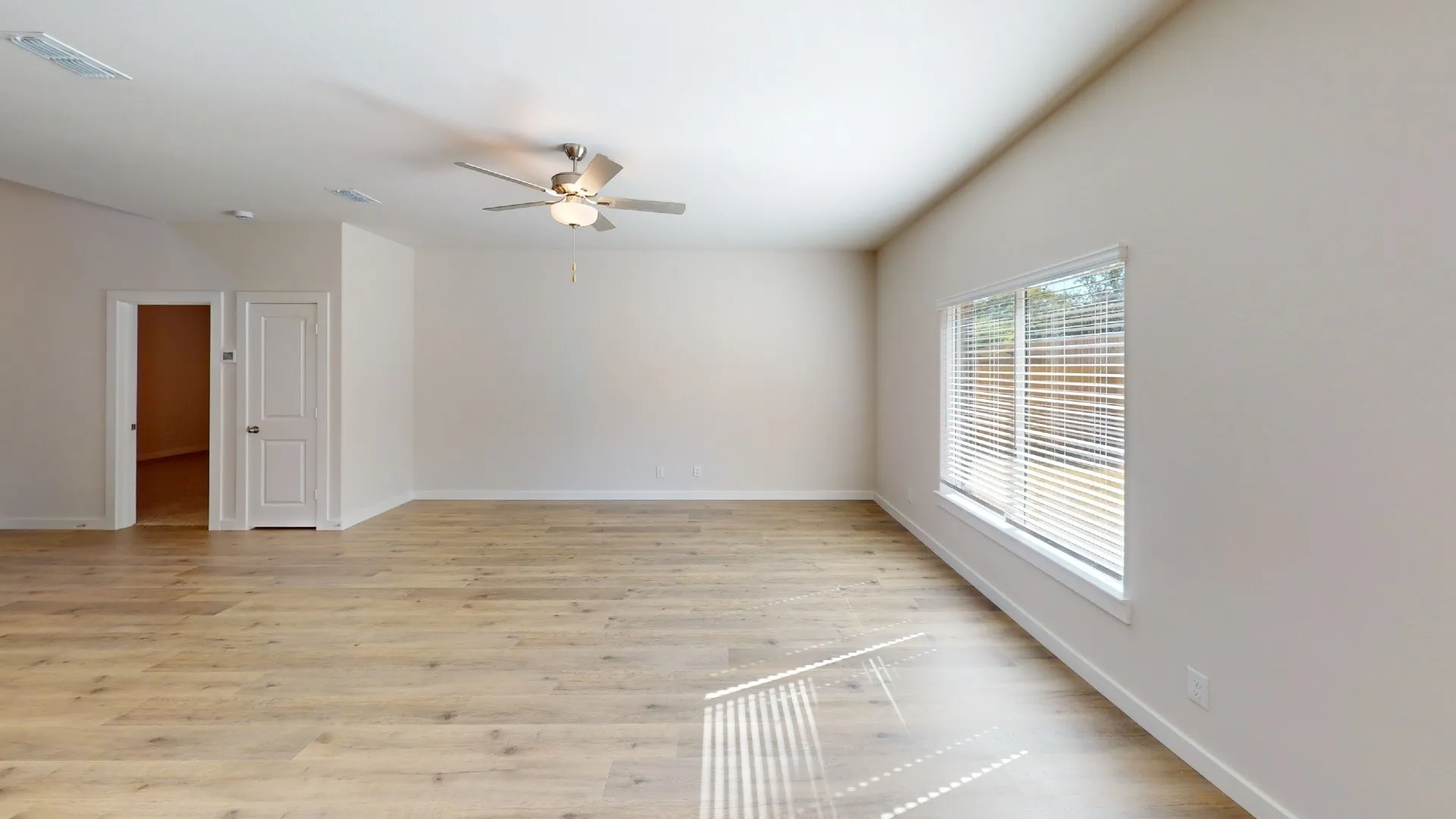 Spacious room with wood-finish flooring, neutral paint, a ceiling fan with integrated lighting, and natural light from a large window