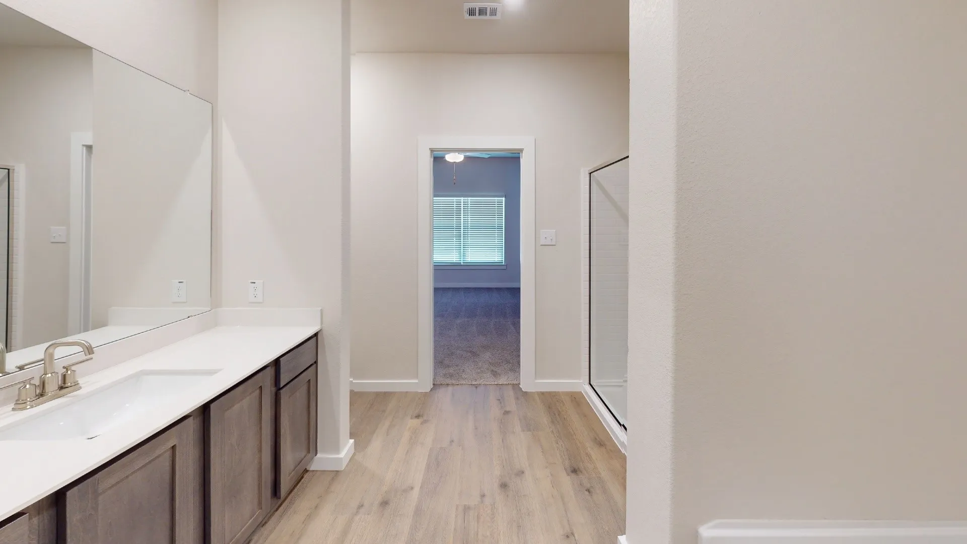 Double vanity with integrated sinks, brushed nickel fixtures, expansive wall mirror, wood-finish flooring, and a glass-enclosed shower
