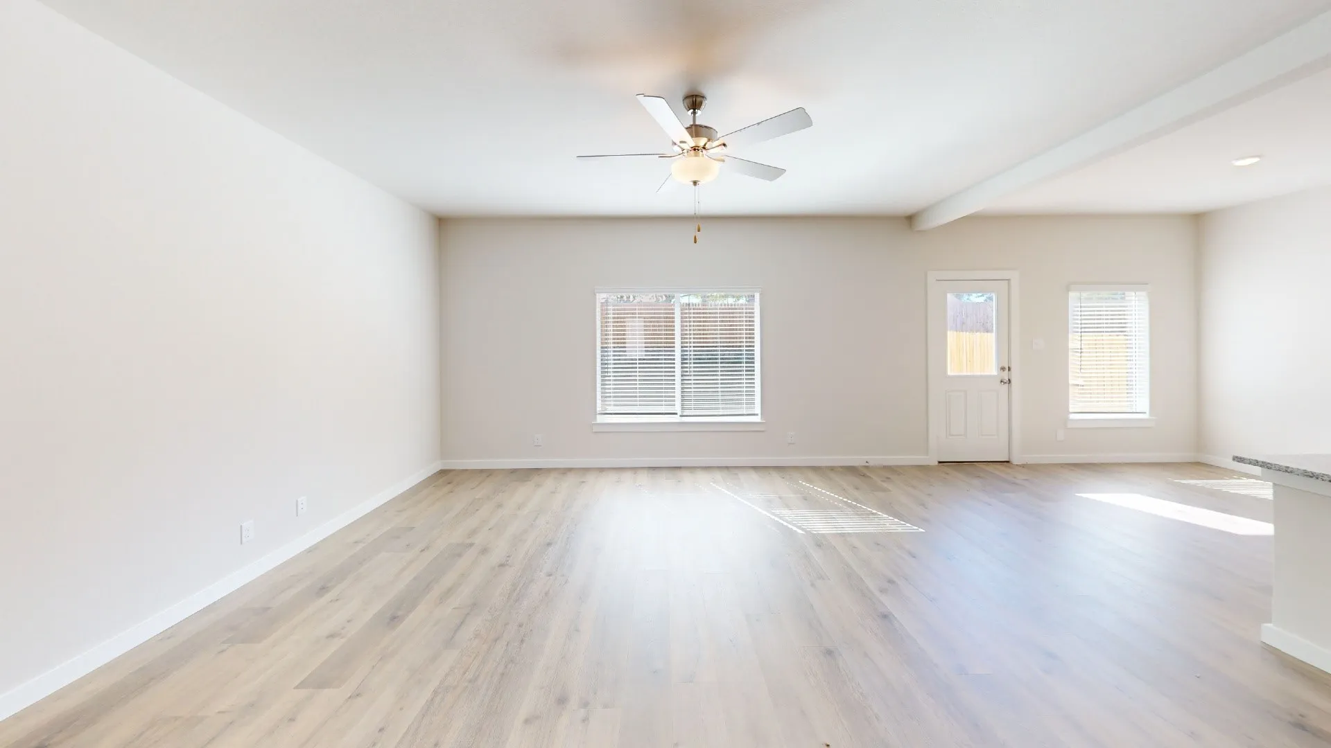 Open-concept living space with wood-finish flooring, a ceiling fan, and multiple windows with blinds