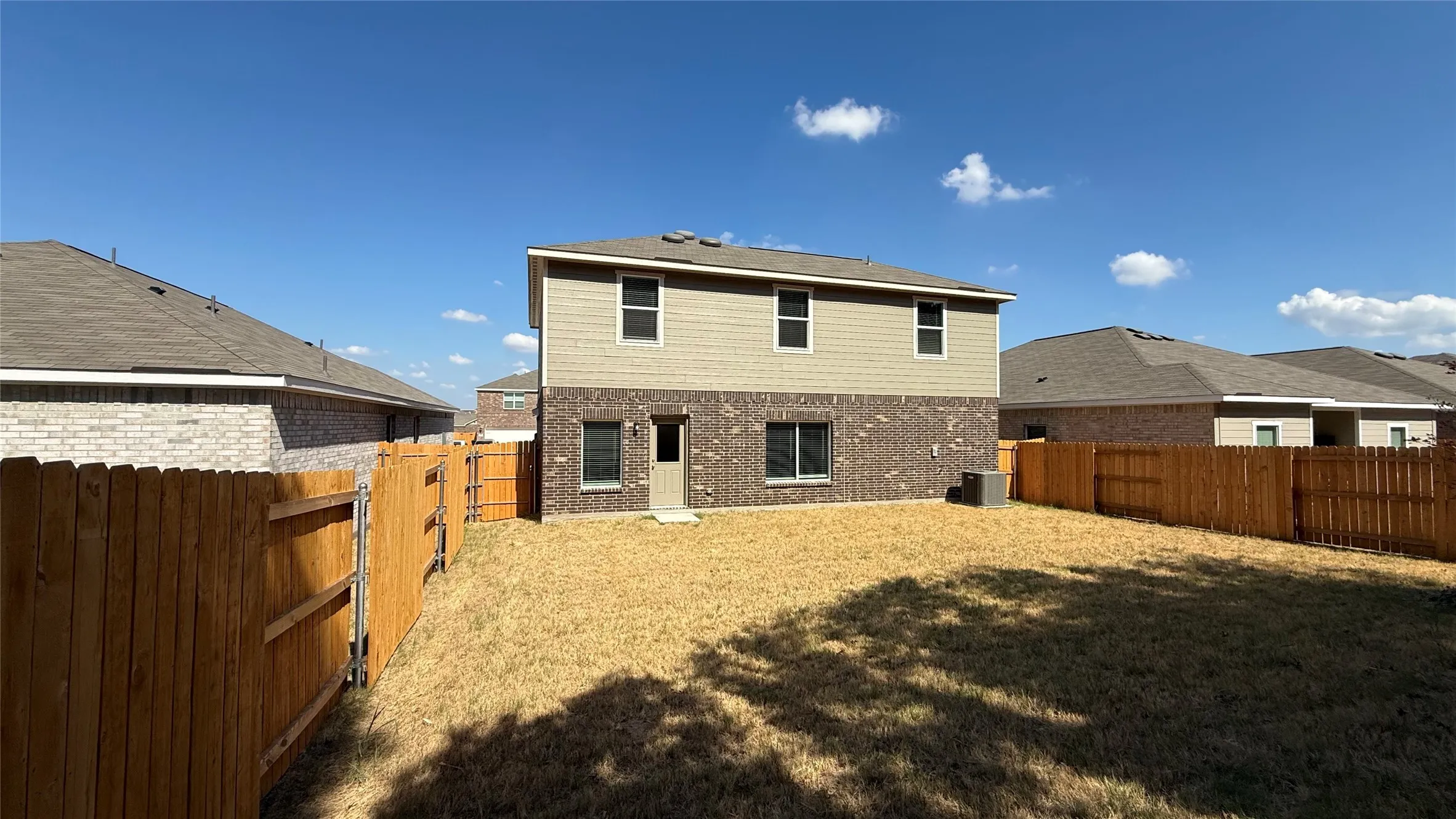 Two-story exterior with brick and siding facade, private wooden fencing, and a spacious yard