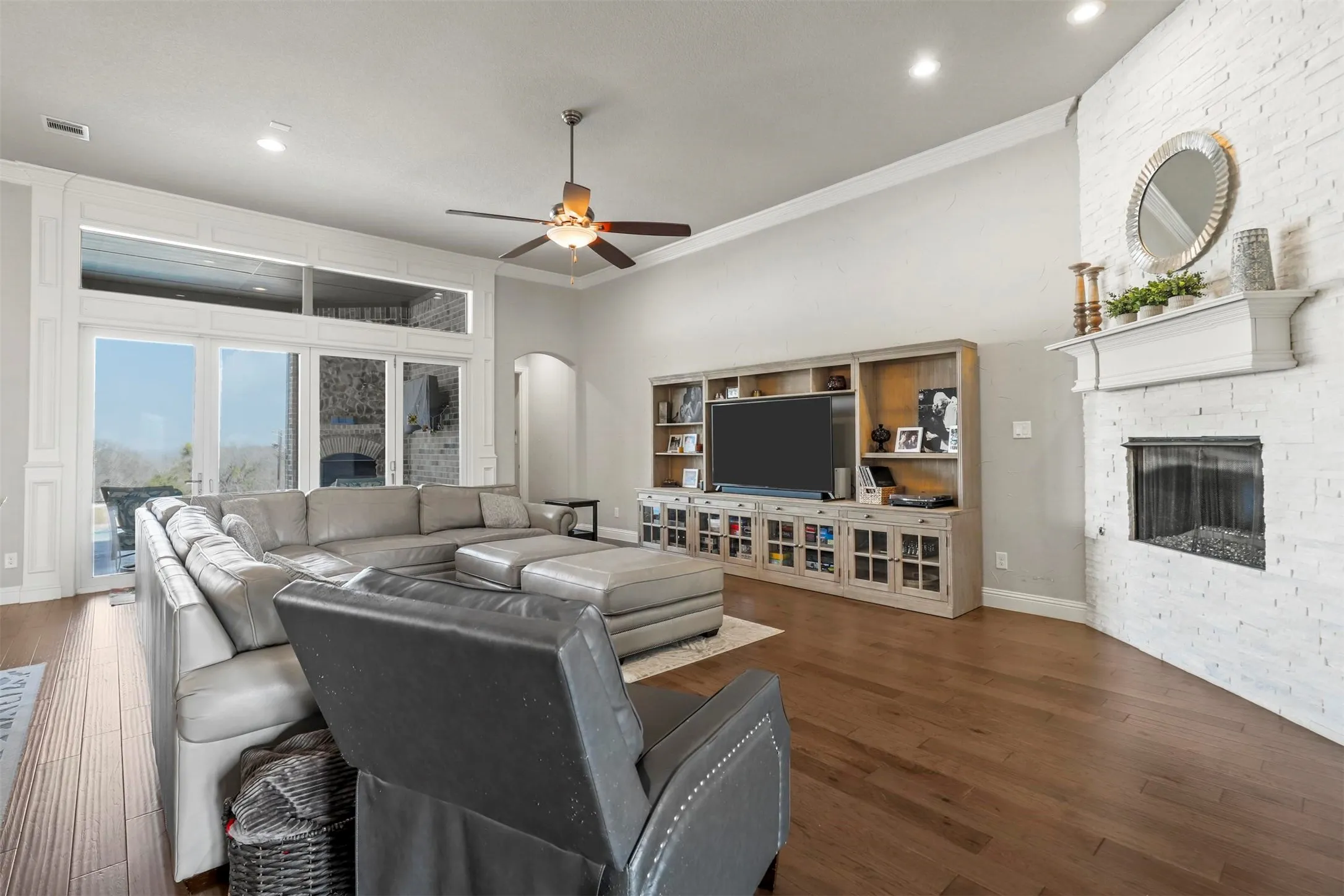 Hardwood flooring, whitewashed brick fireplace with mantel, built-in entertainment center, high ceilings, and recessed lighting