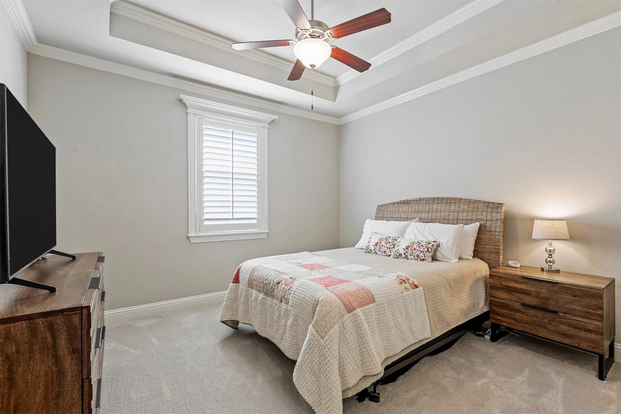 Tray ceiling with crown molding and a ceiling fan, plantation shutters, and light-toned carpeting