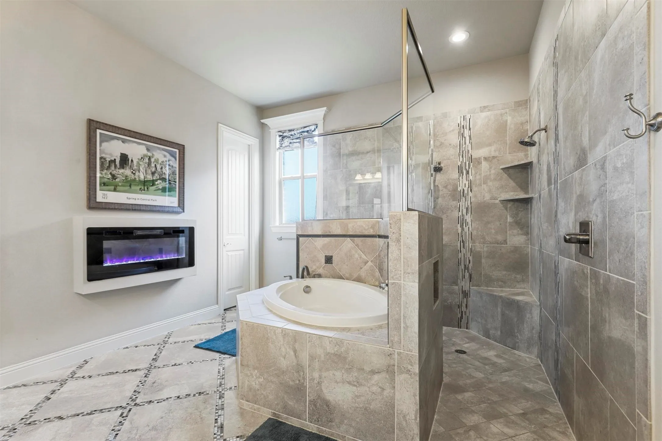 Spa-inspired primary bathroom featuring a freestanding soaking tub, walk-in shower with frameless glass enclosure and linear tile detailing, dual vanity with vessel sink, heated floor system, recessed lighting, and stone-finish tile throughout