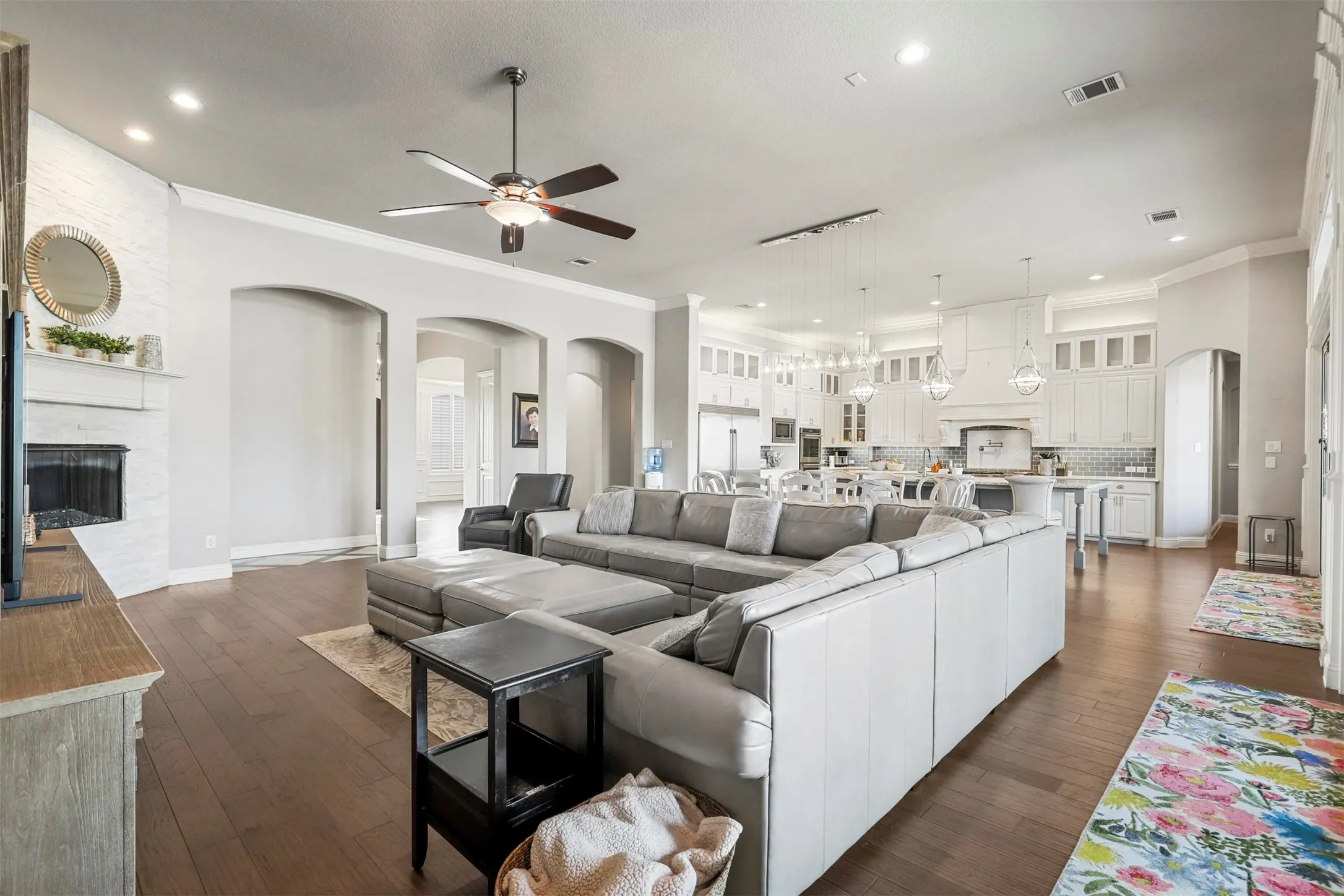 Expansive open-concept living area featuring wood-finish flooring, a white brick fireplace, recessed lighting, and a ceiling fan