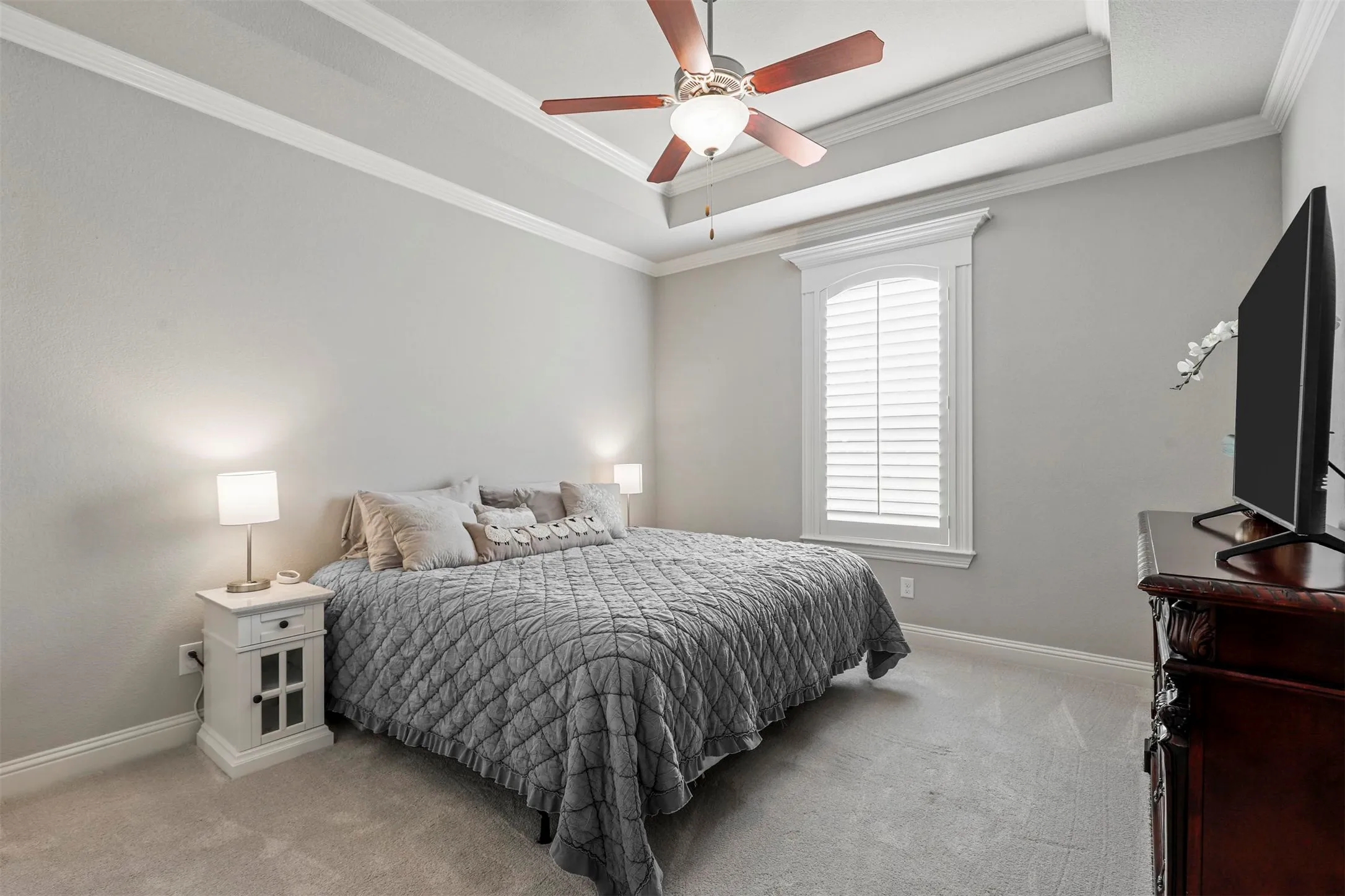 Tray ceiling with ceiling fan, white window shutters, and light gray wall paint