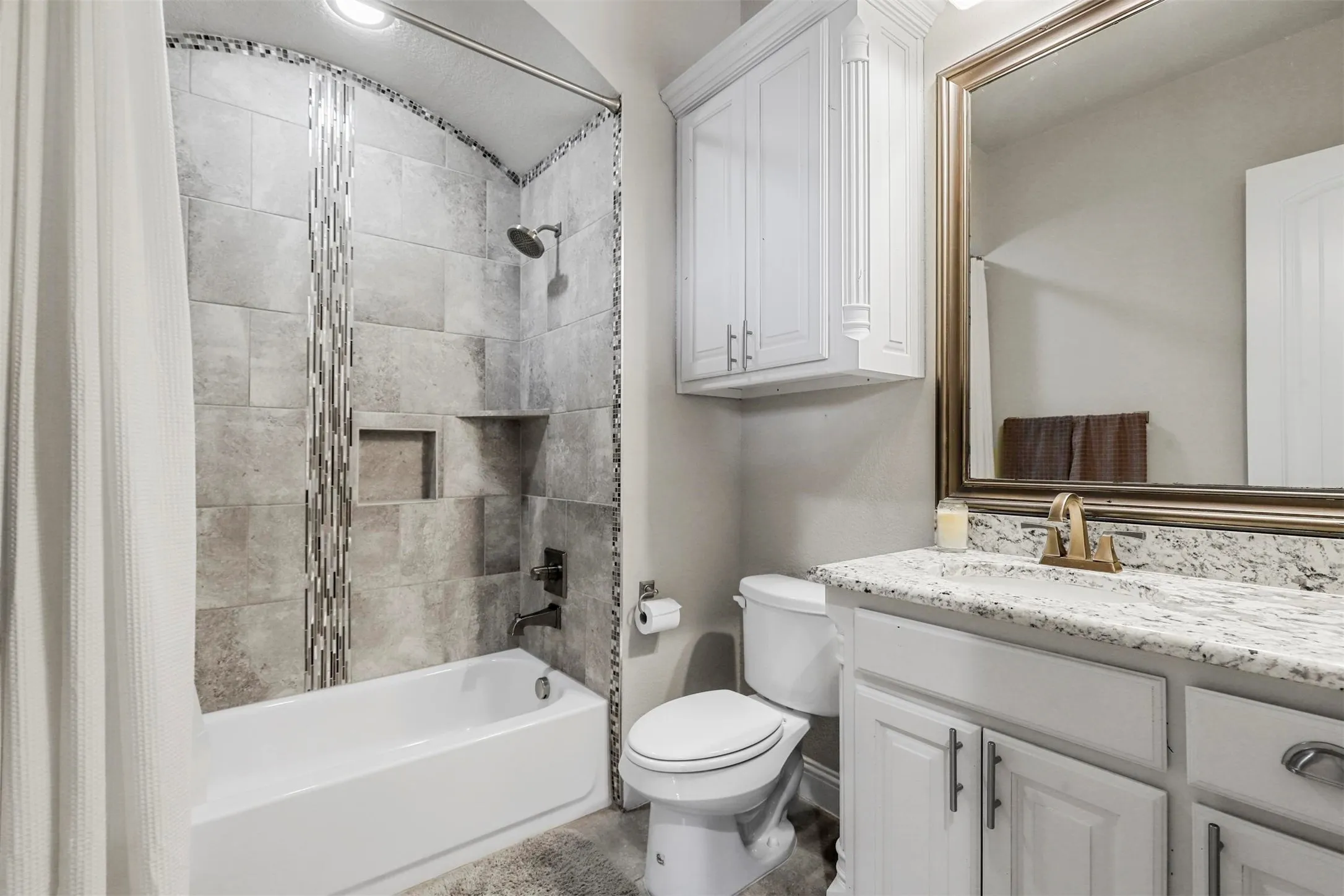 Tub and shower combination featuring tiled walls, built-in shelving, and a decorative tile accent strip