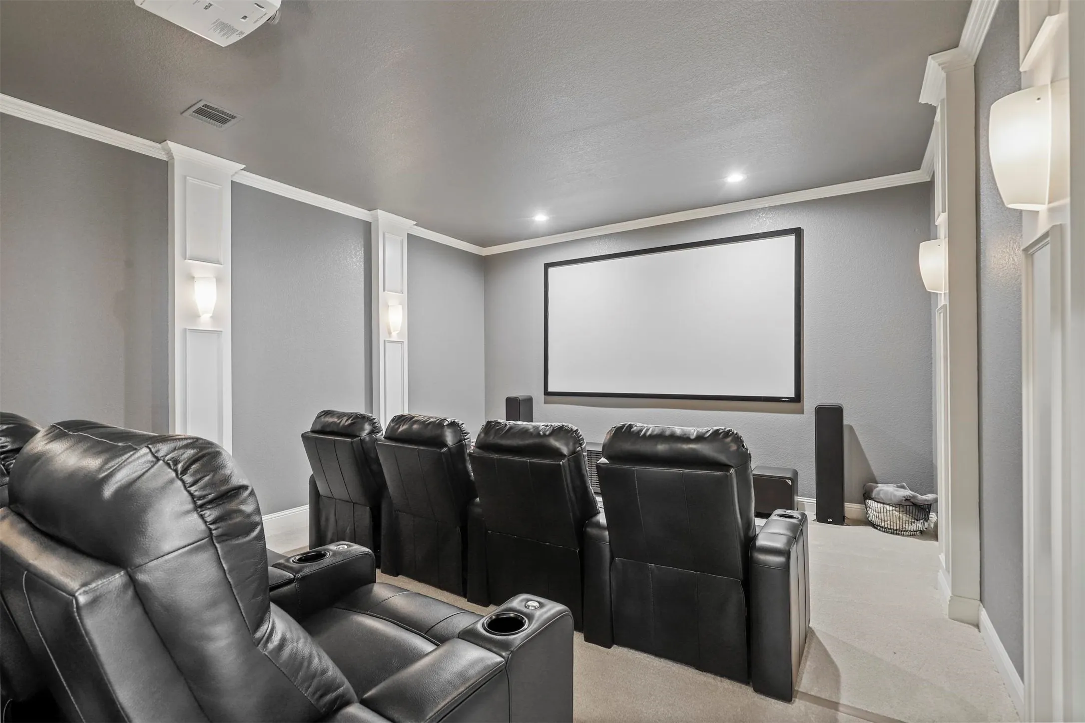 Media room with a large projection screen, recessed lighting, and decorative wall sconces
