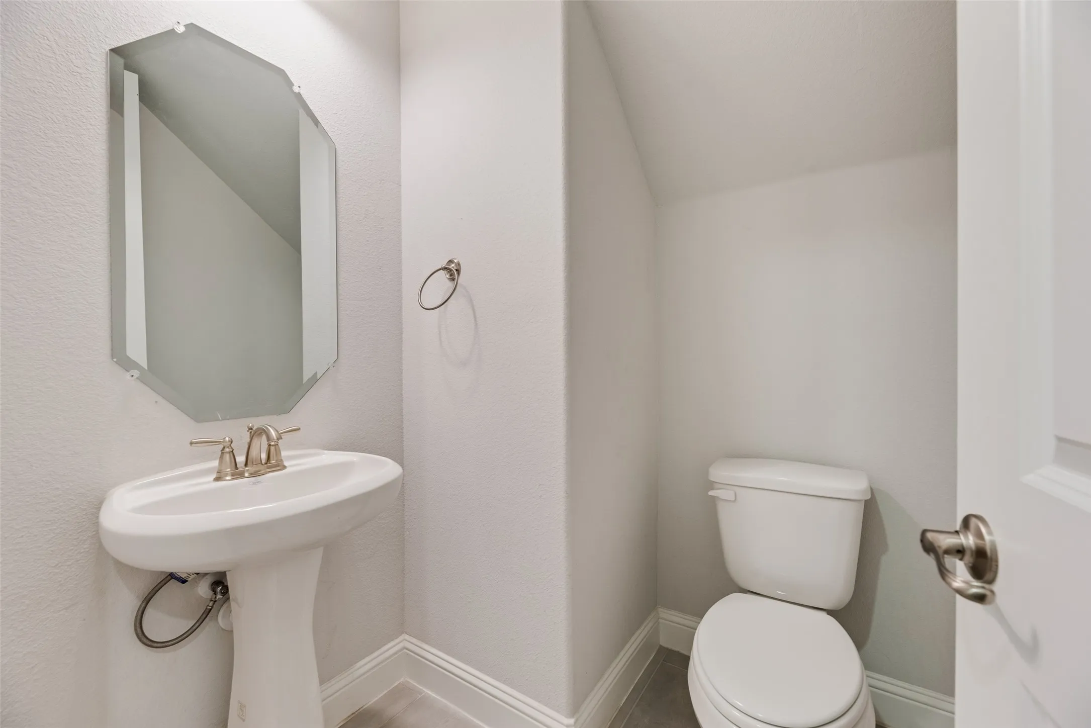 Pedestal sink with brushed nickel faucet, geometric mirror, and white baseboards