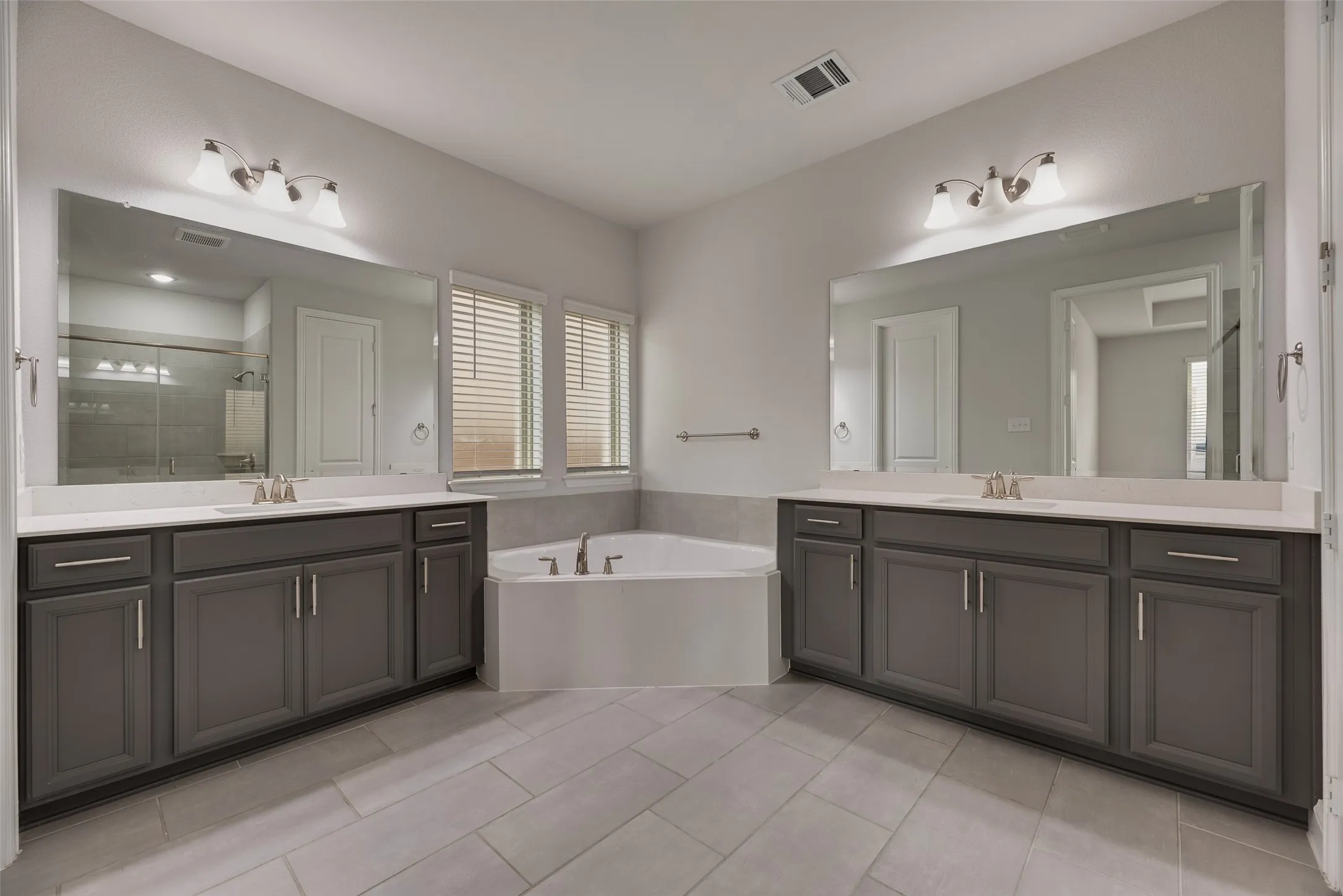 Corner soaking tub with dual vanity stations featuring gray cabinetry and white countertops