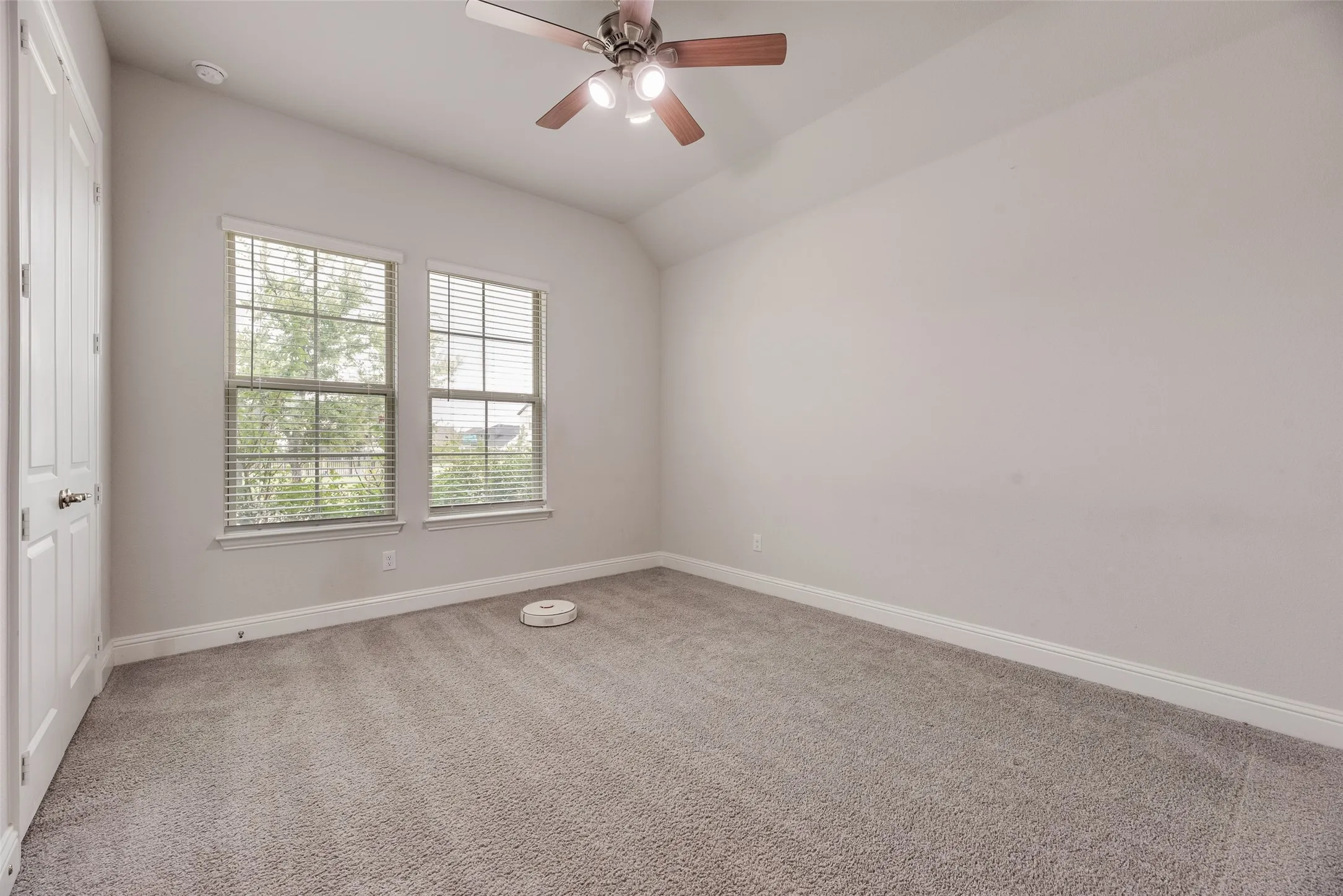 Carpeted room featuring two windows with horizontal blinds, a ceiling fan with integrated lighting, and a white paneled door