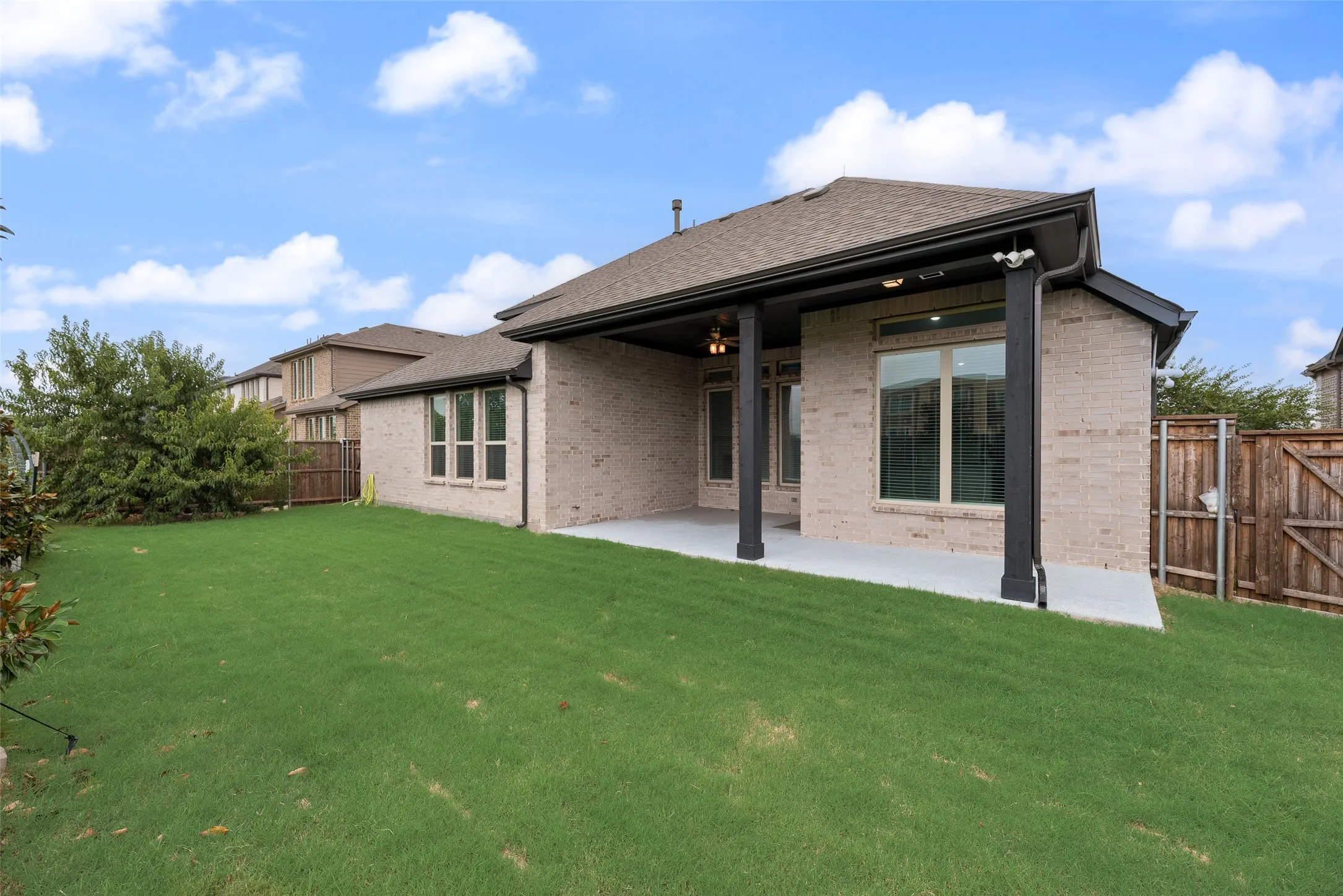 Expansive green lawn with a covered patio, light brick exterior, and dark trim