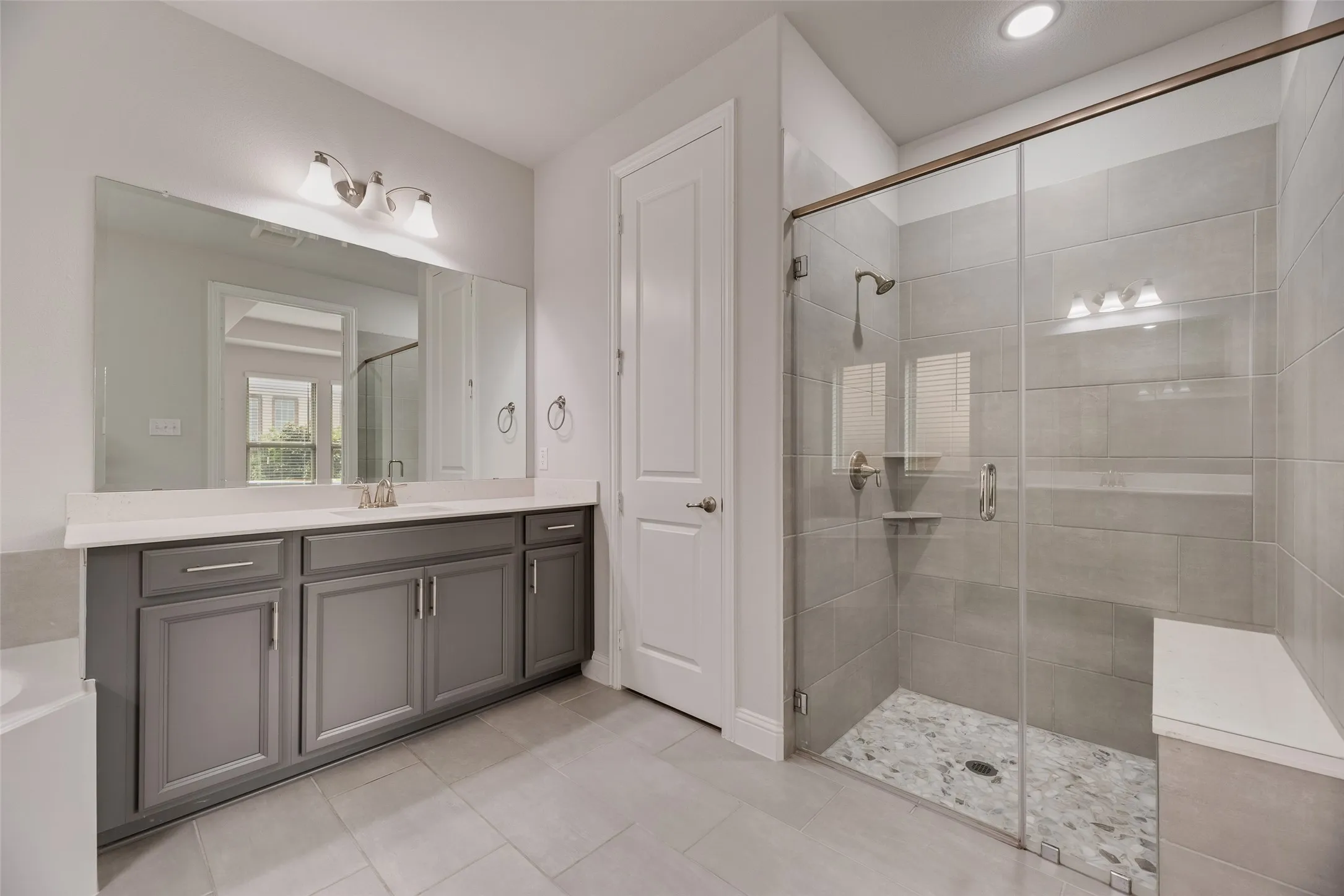 Spacious bathroom featuring a glass-enclosed shower with pebble-finish flooring and a built-in bench