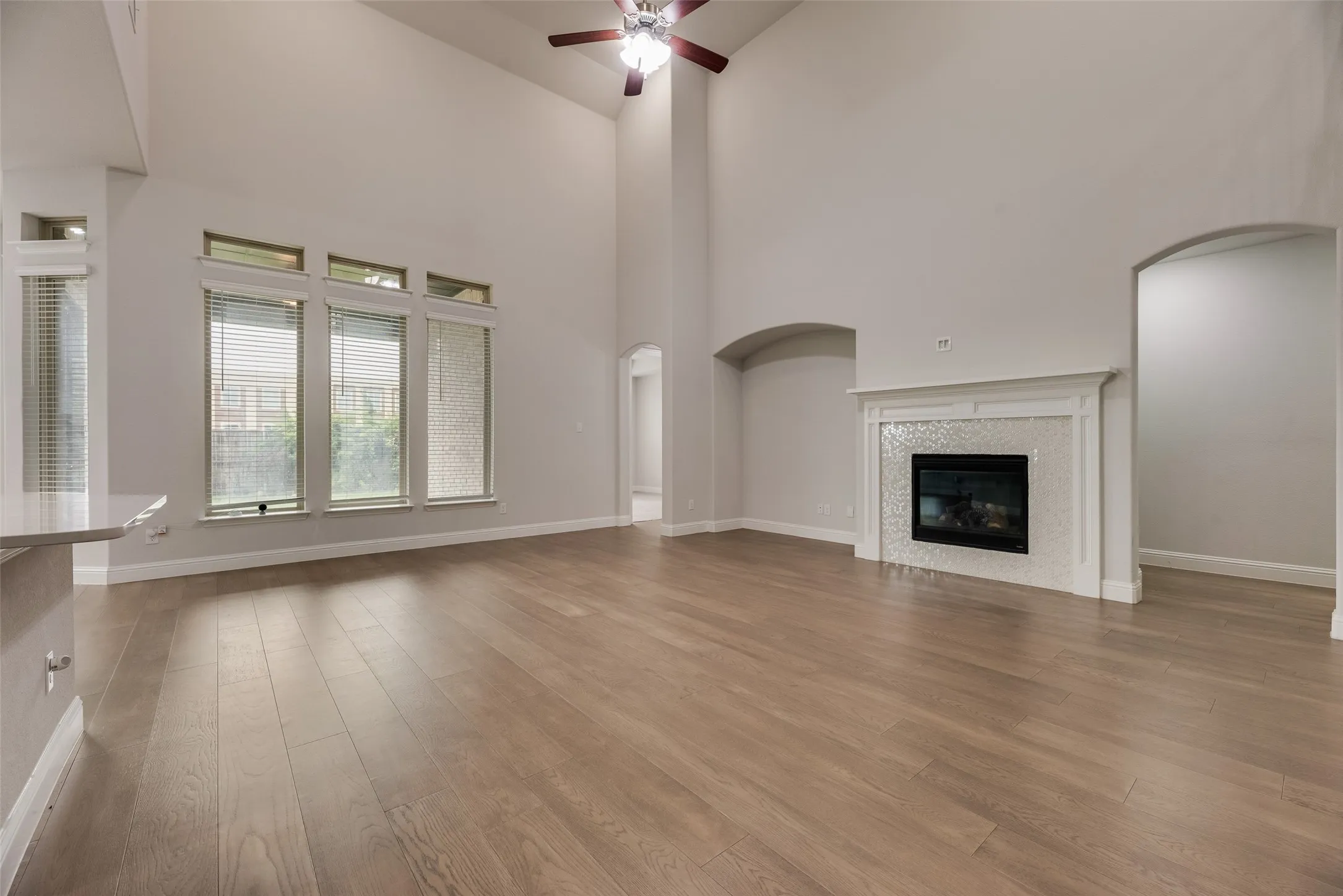 Vaulted ceiling living area featuring wood-finish flooring, a contemporary fireplace with a decorative tile surround, arched wall features, and a ceiling fan
