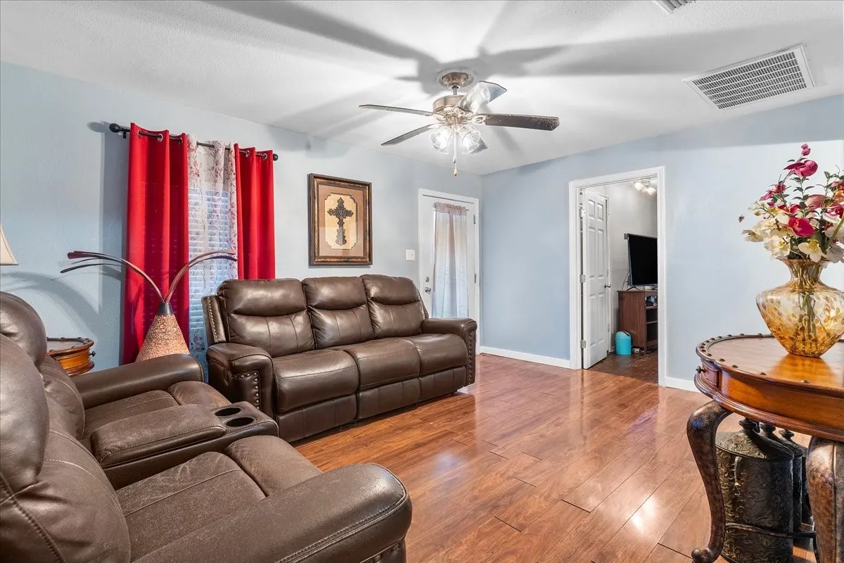 Wood-finish flooring, light blue wall paint, ceiling fan with integrated lighting, white trim, and a white interior door