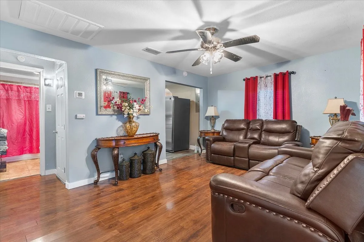 Spacious interior with wood-finish flooring, a ceiling fan with integrated lighting, and light blue walls