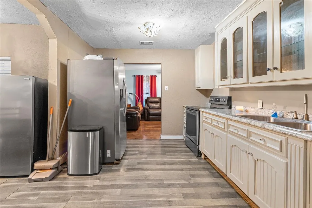 Kitchen featuring wood-finish flooring, cream-toned cabinetry with glass-front uppers, and stainless steel appliances