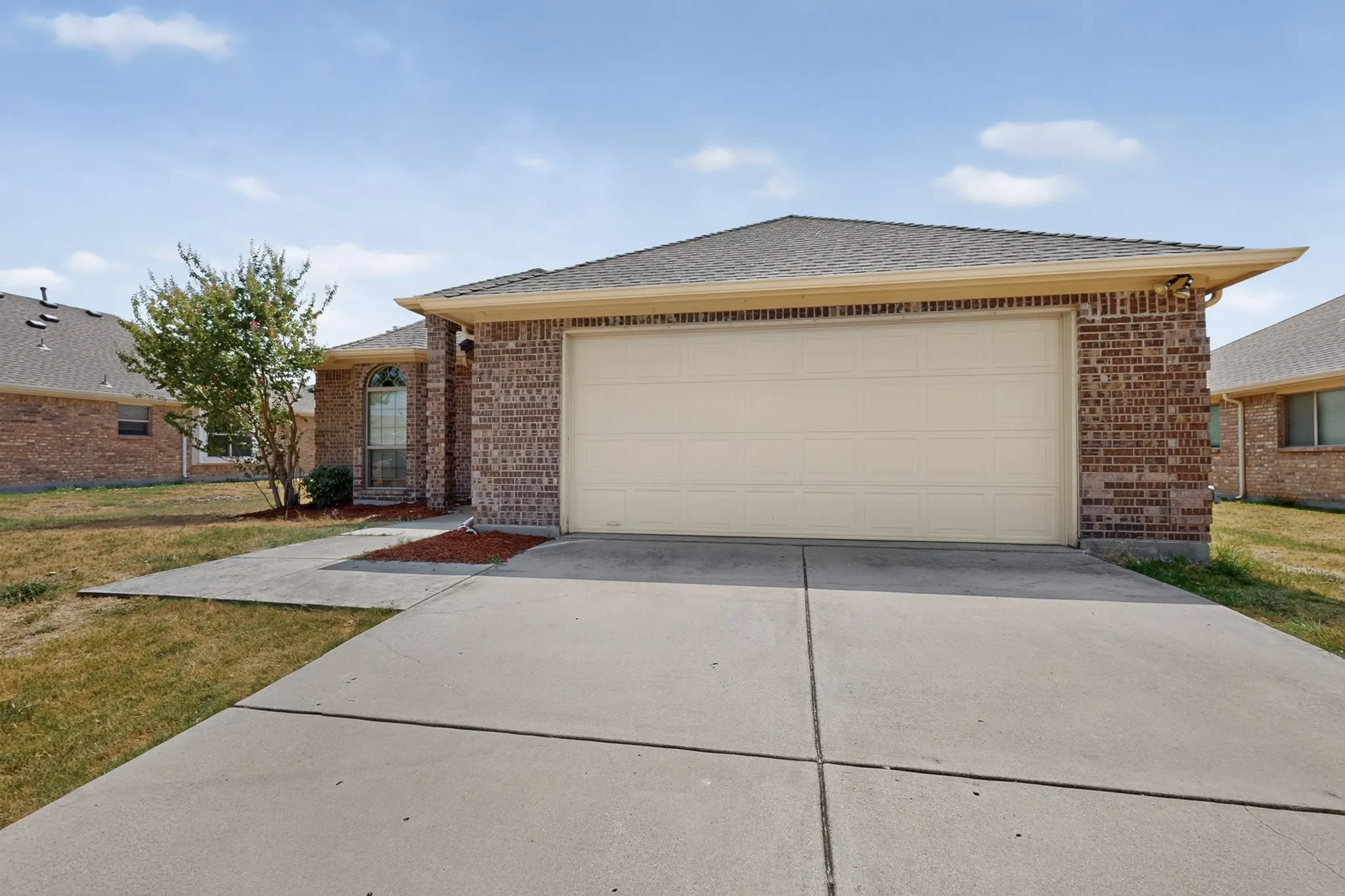Brick exterior with a single-car garage, concrete driveway, and a small front yard with a tree