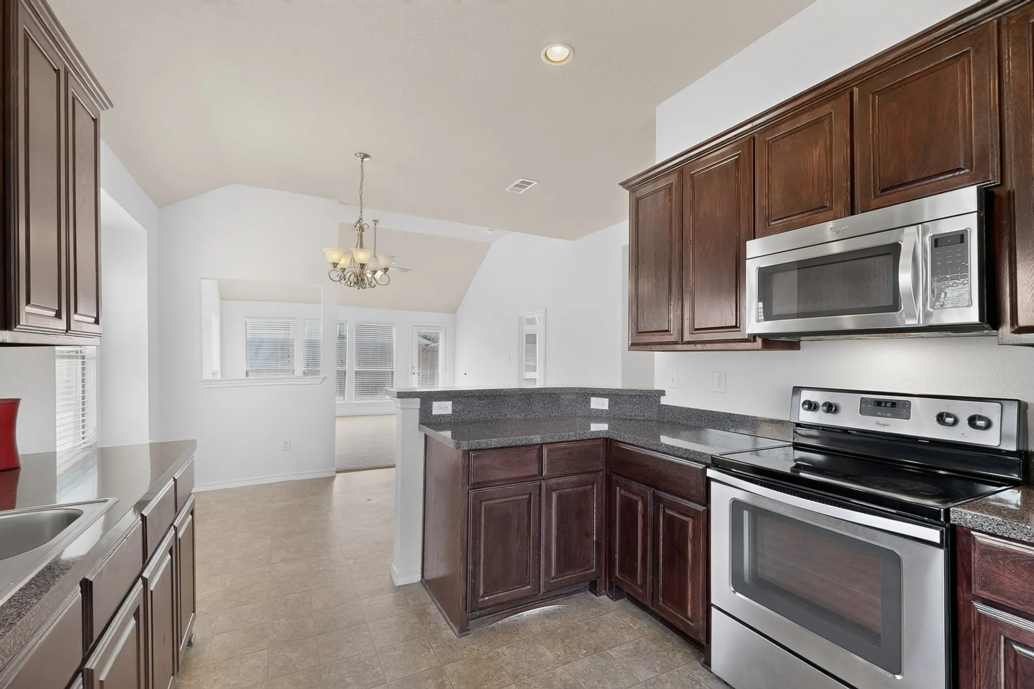 Dark wood-finish cabinetry, stainless steel appliances, dark stone-finish countertops, and an integrated kitchen sink