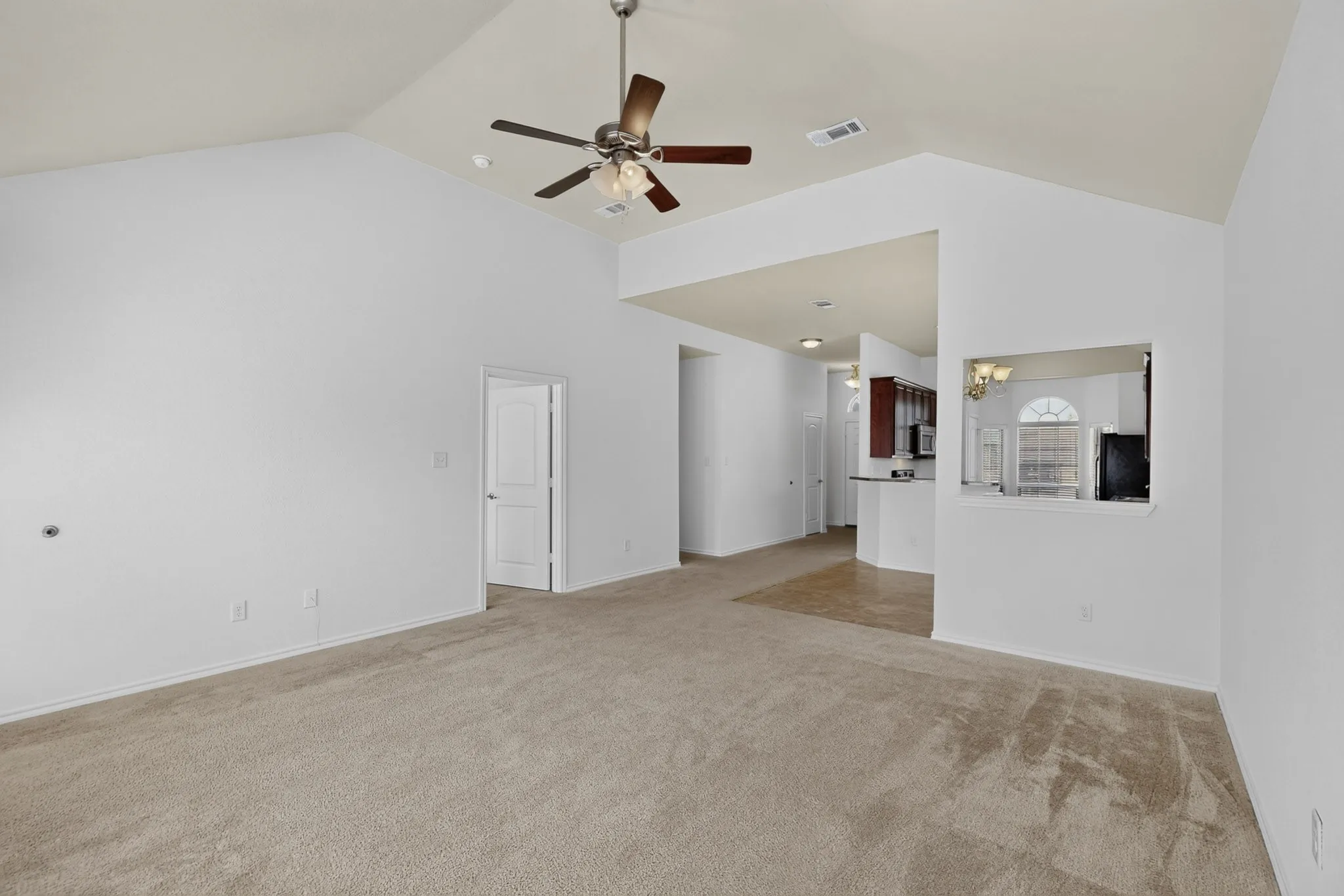 Vaulted ceiling with a ceiling fan, neutral carpet flooring, pass-through window, wood-finish cabinetry, and recessed lighting