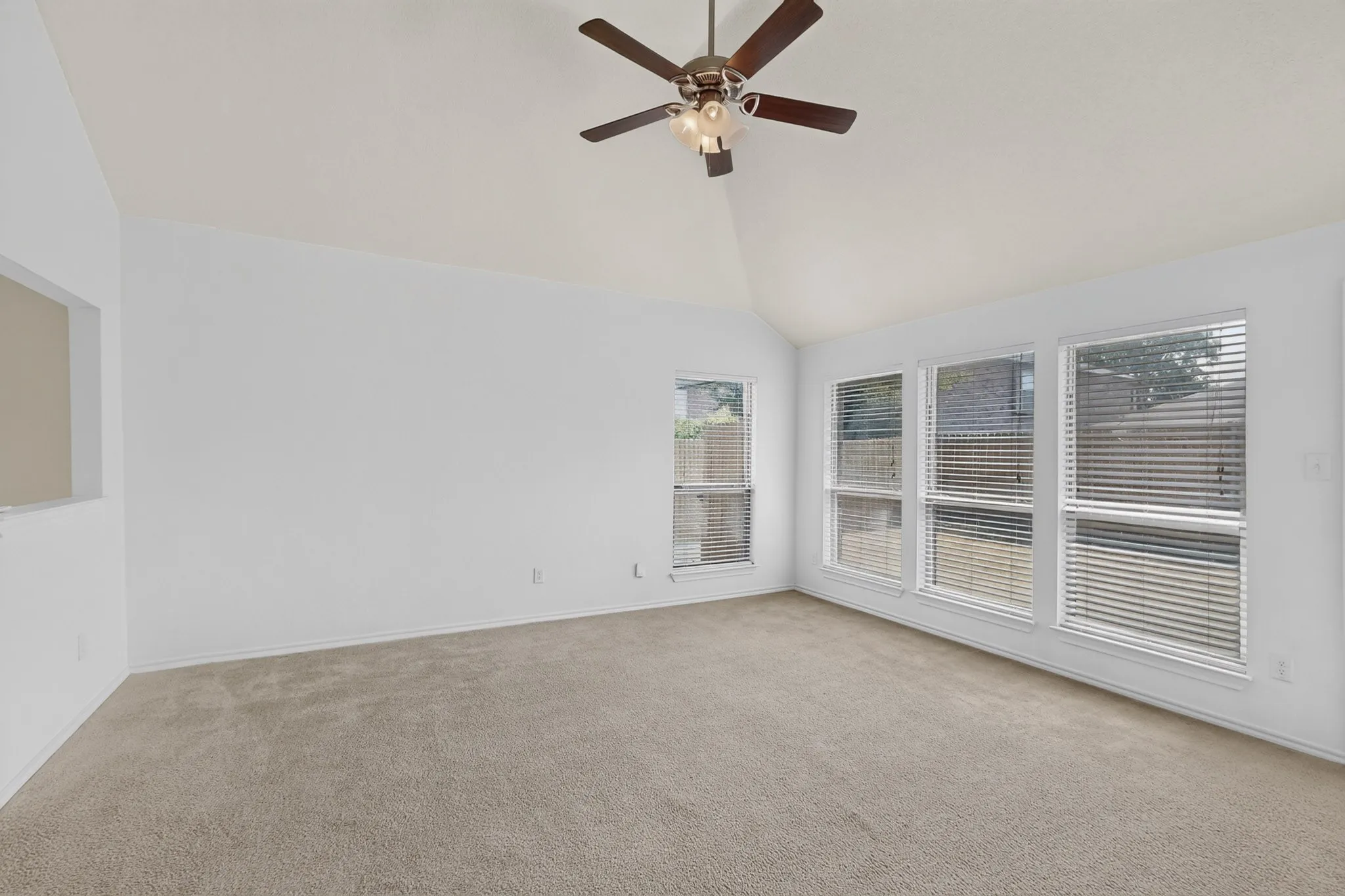Vaulted ceiling with a ceiling fan, light neutral carpet, and multiple windows