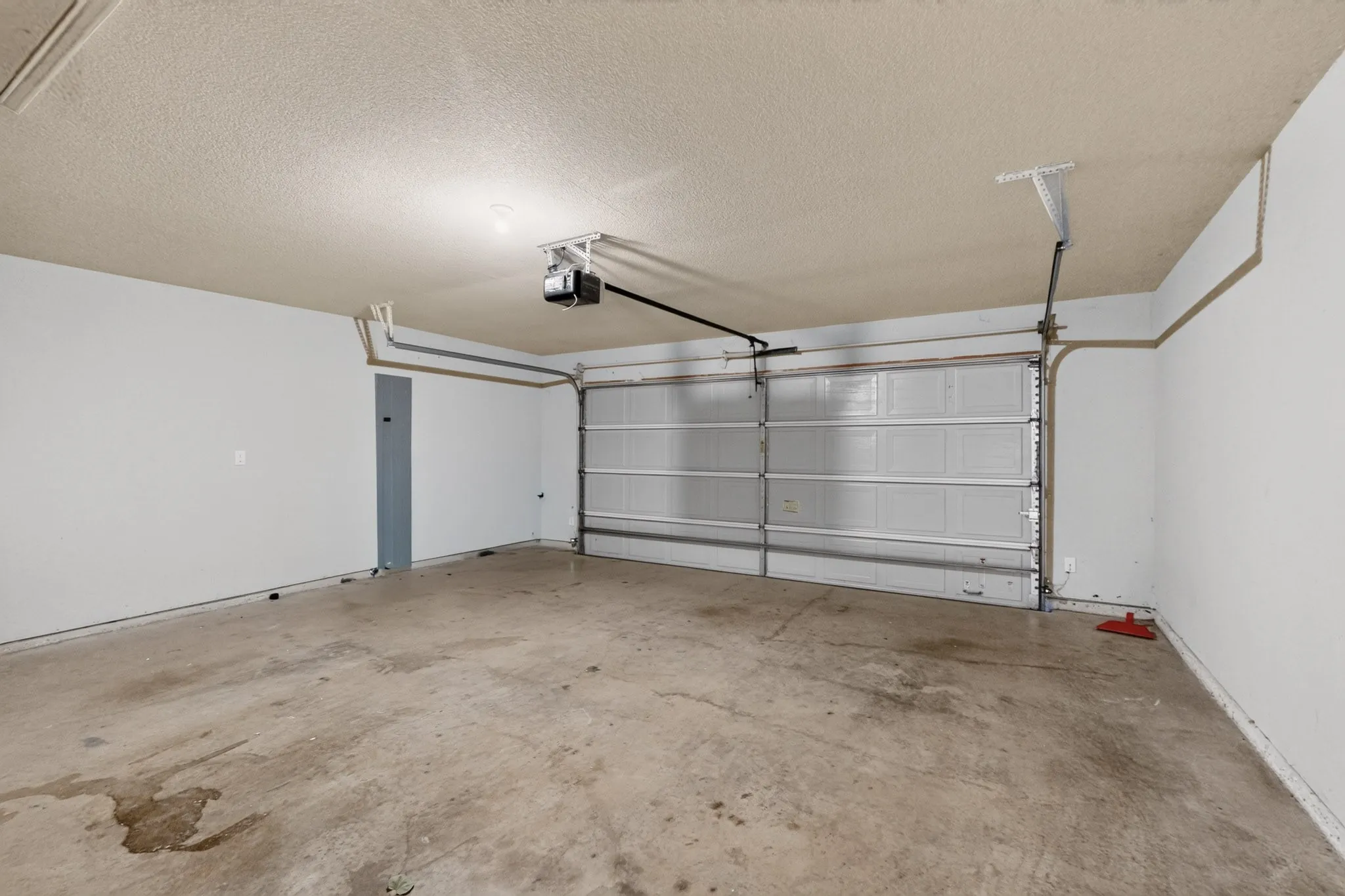 Integrated garage with a roll-up door, exposed ceiling-mounted garage door opener, and textured ceiling