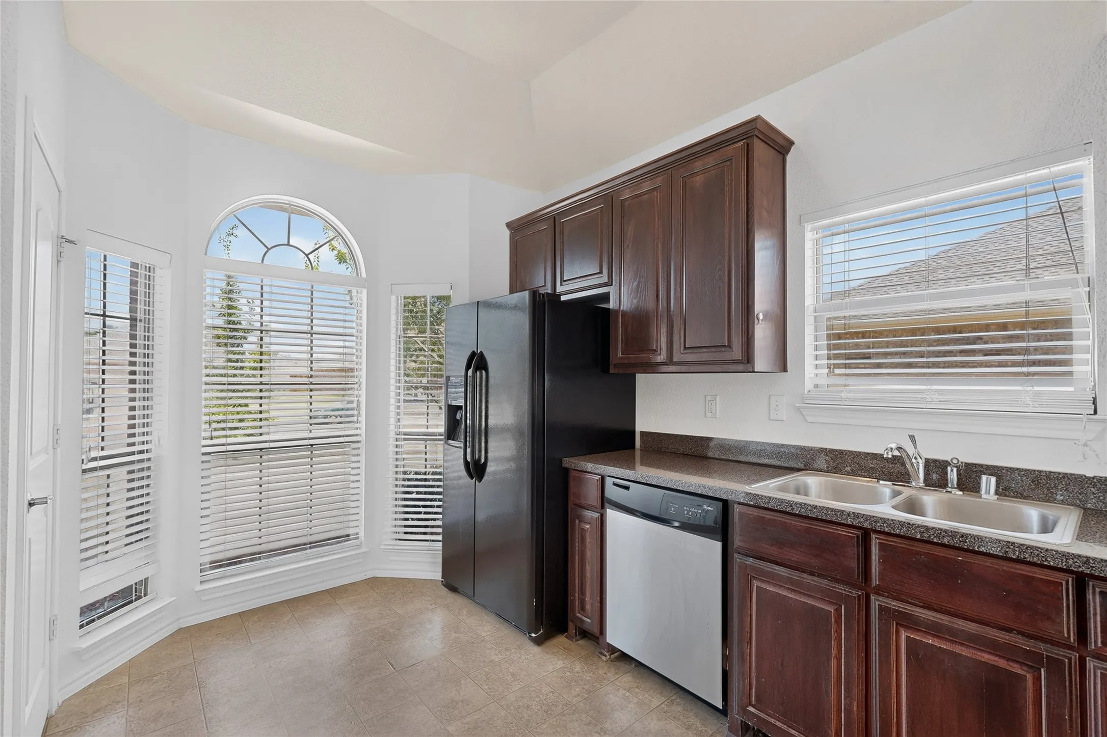 Kitchen featuring dark wood cabinetry, a stainless steel double basin sink, and a black side-by-side refrigerator