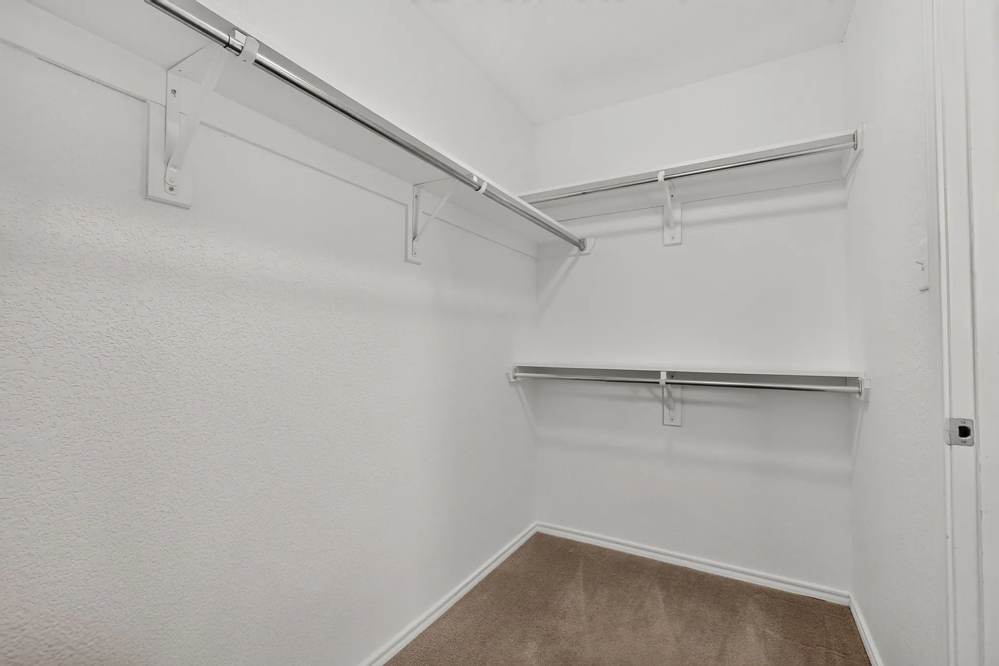 Walk-in closet featuring white wire shelving, chrome rods, textured walls, and carpet flooring