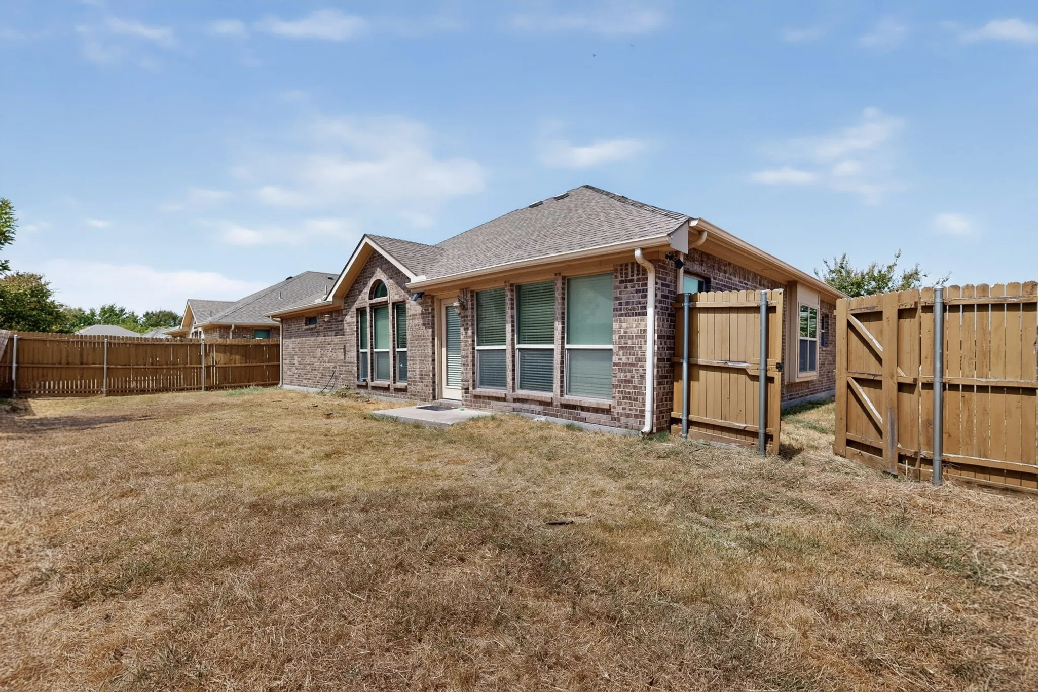 Brick exterior featuring a wood fence, multiple windows, and a patio