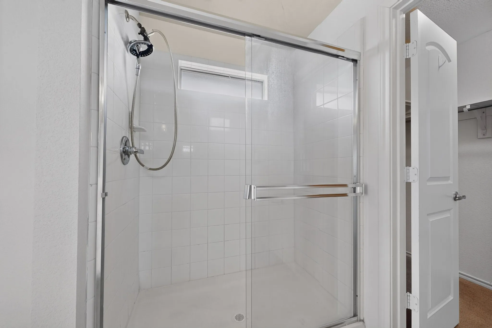 Shower enclosure with sliding glass door and white square tile surround