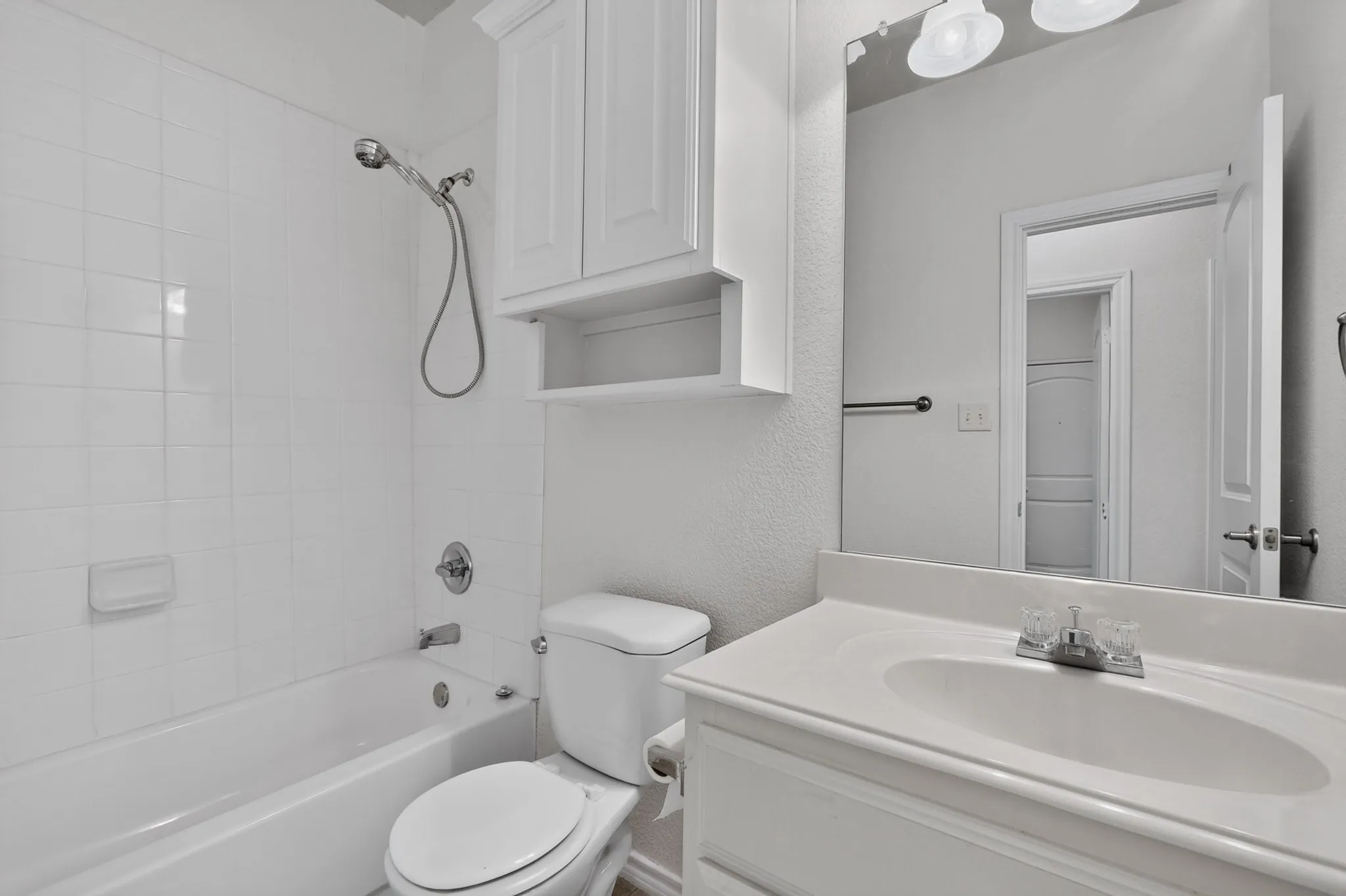 Bathroom featuring a white vanity with integrated sink, white cabinetry, a tub-shower combination with white subway tile, and a wall-mounted mirror