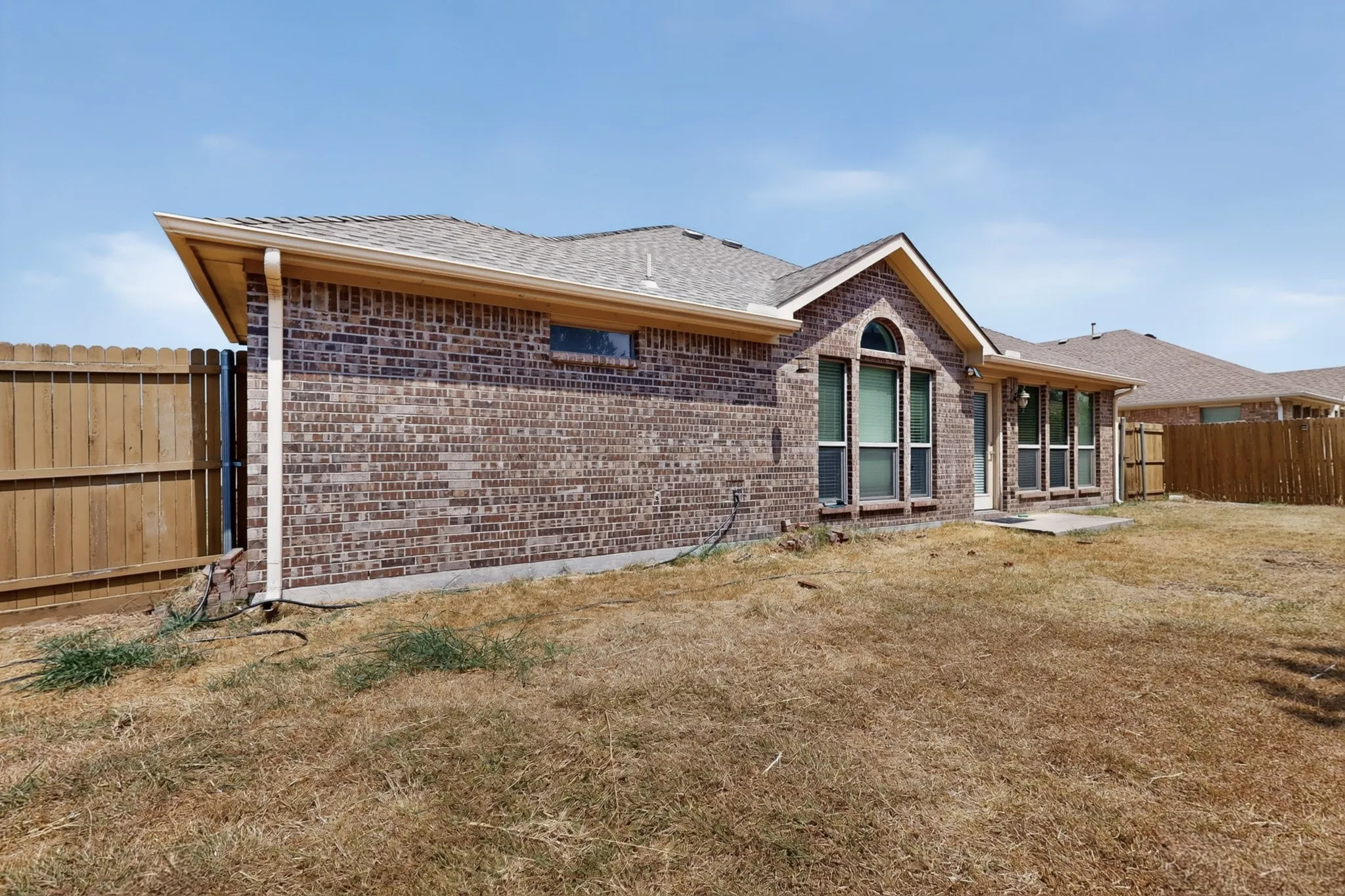 Brick exterior with arched window, multiple large windows, covered patio area, and private fenced yard