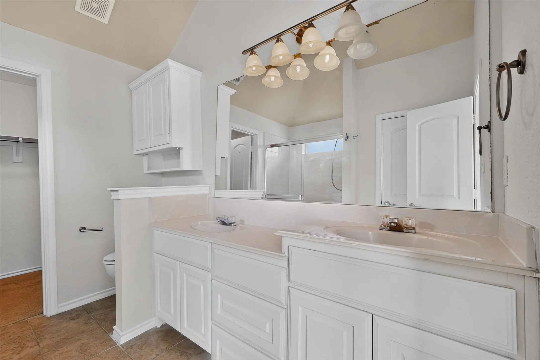 Double vanity with integrated sinks, white cabinetry, wall-mounted mirror, and decorative light fixture